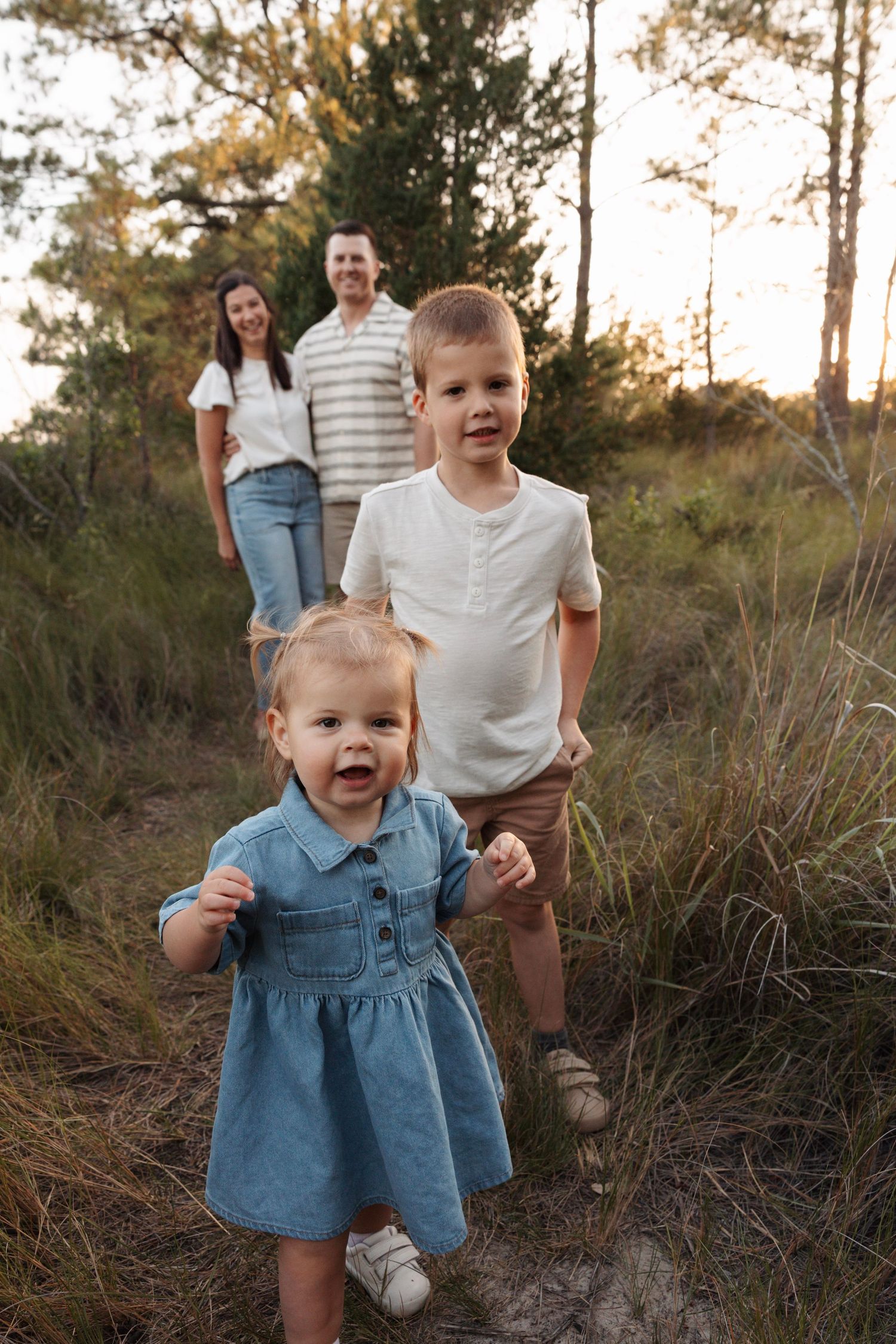 Young family with two children walking on sandy forest trail during golden hour sunset.