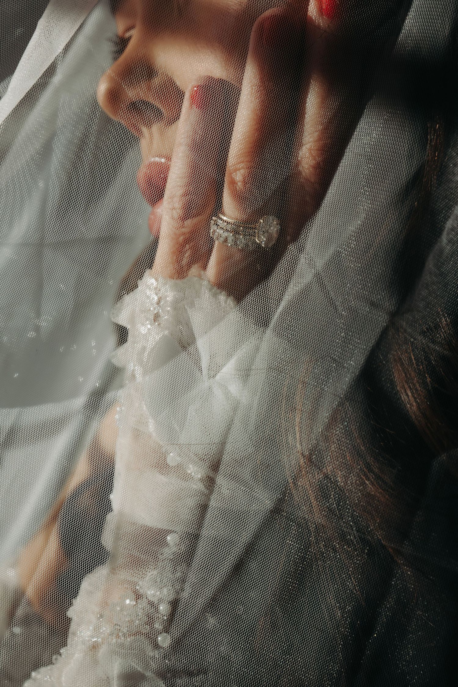 Close-up of bride wearing a diamond wedding ring while holding her veil near her face.