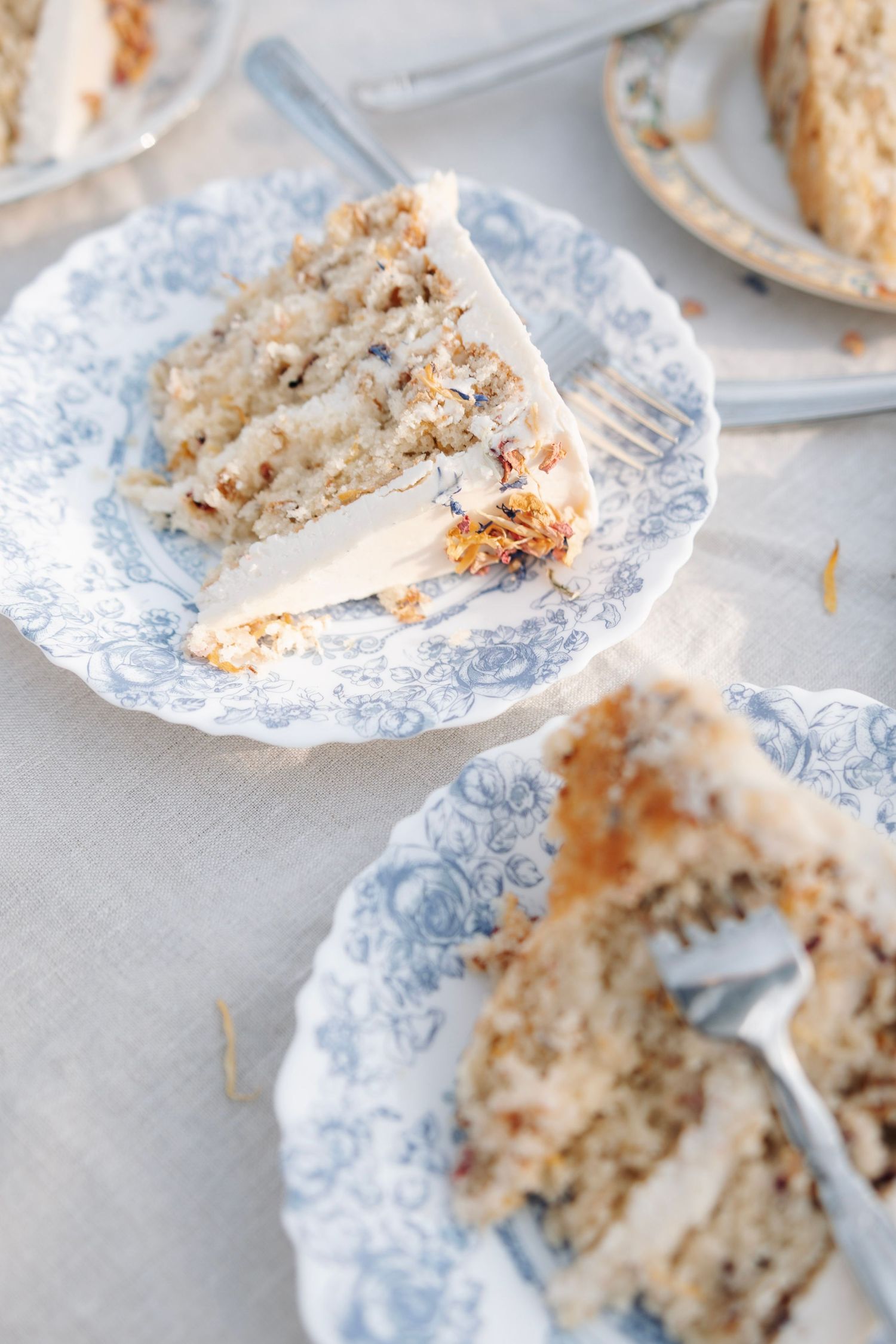 Slices of layered white frosted cake with nuts served on blue and white floral china plates.