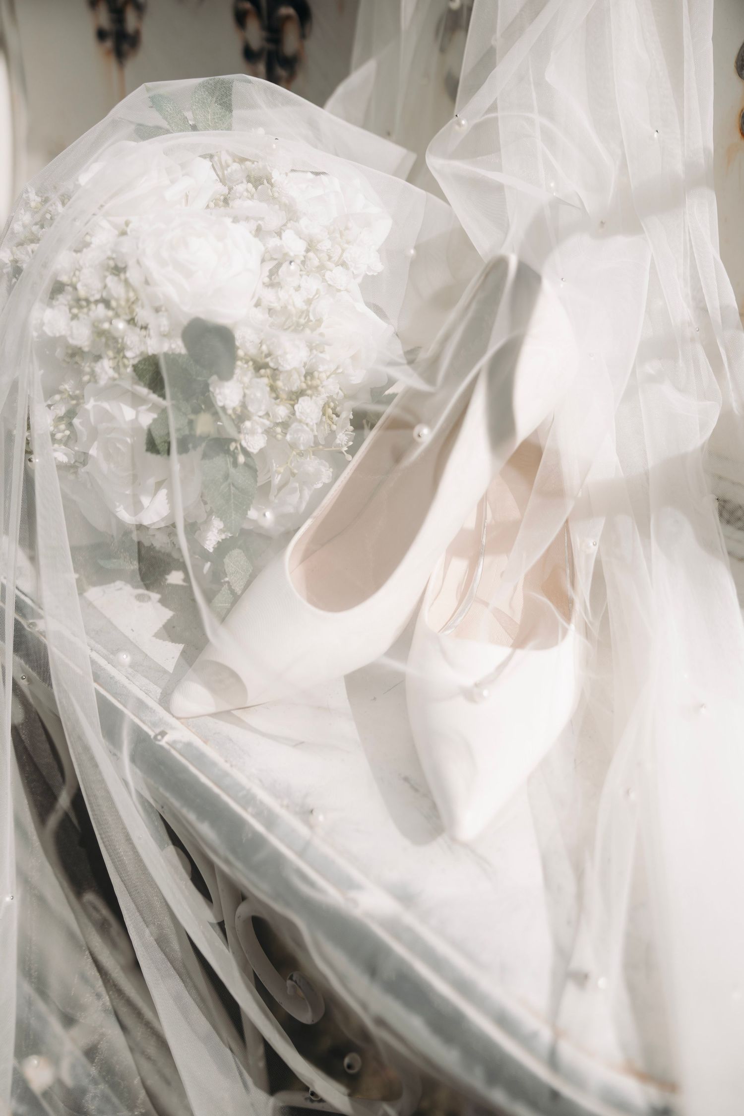 White bridal heels and floral bouquet draped under sheer wedding veil.
