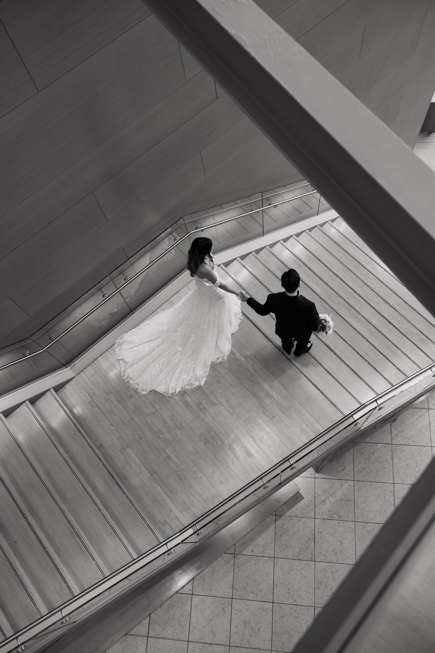 Aerial black and white photo of bride and groom holding hands on elegant staircase.