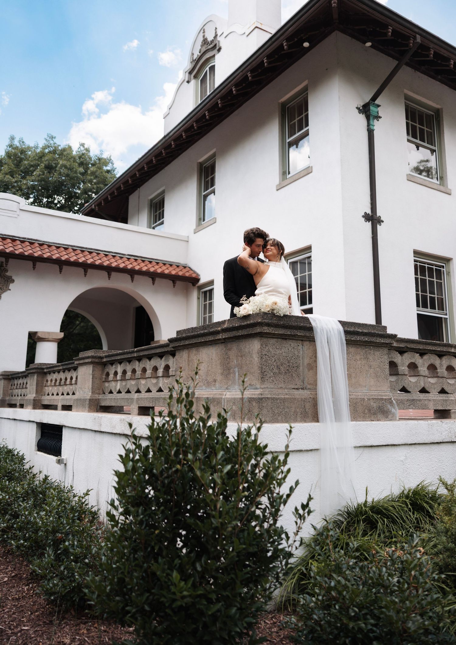 Bride and groom sharing a kiss on a balcony of a white Spanish-style mansion.