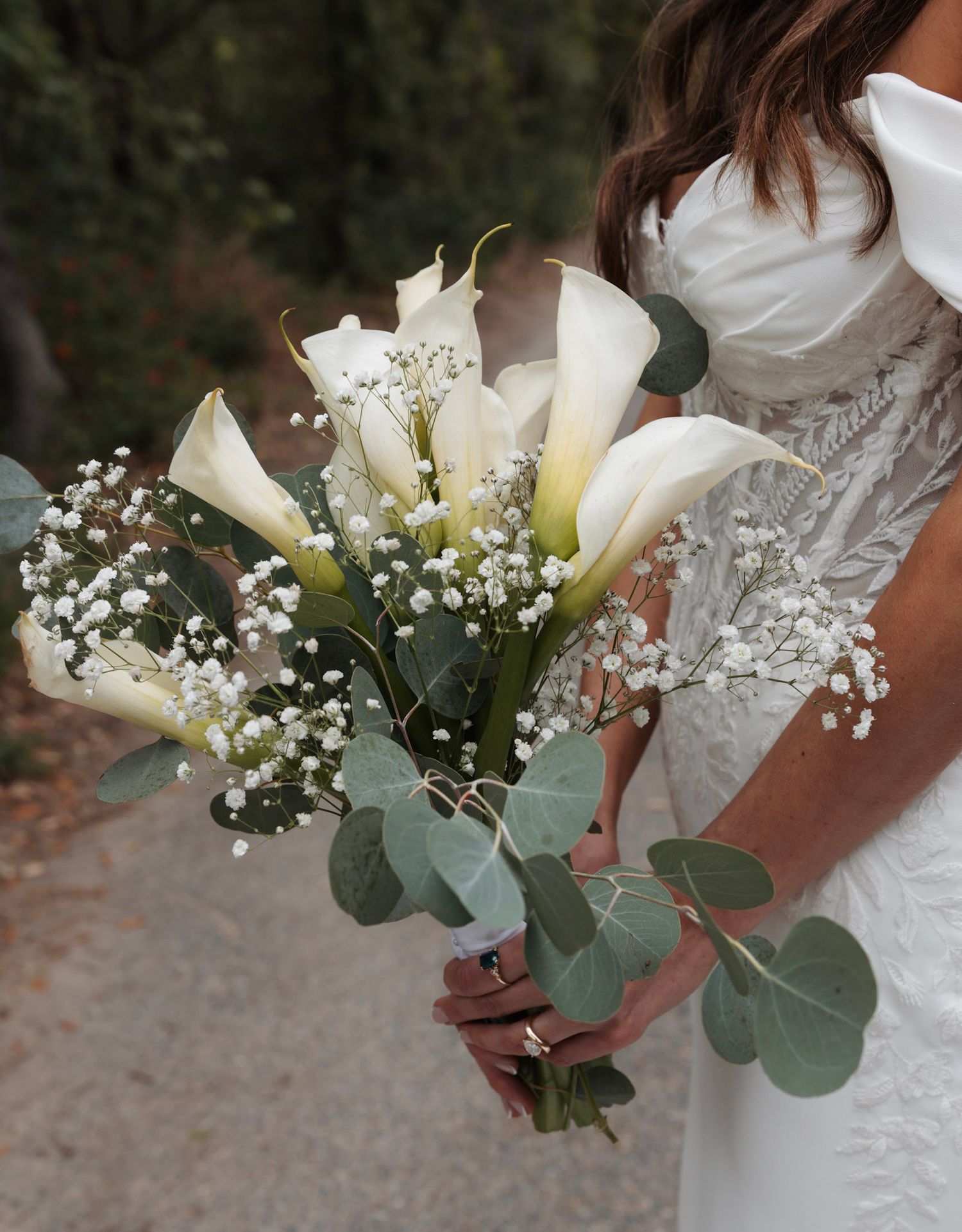Bride holding elegant bouquet of white calla lilies, baby's breath, and eucalyptus leaves.