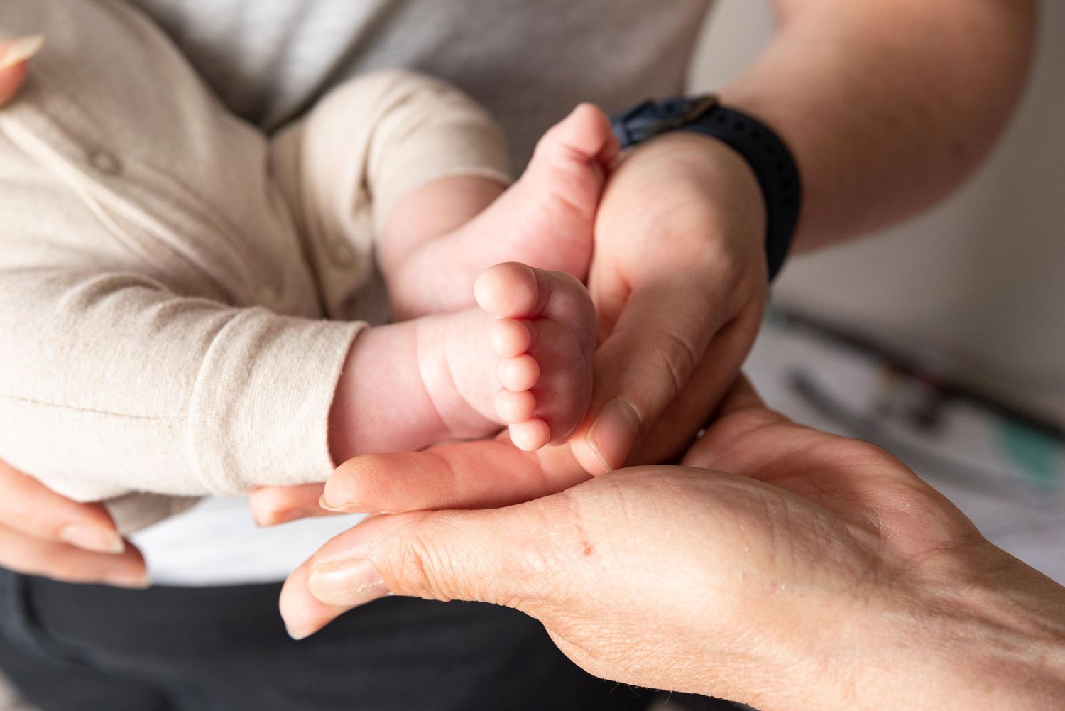Des mains d'adultes bercent délicatement les petits pieds d'un nouveau-né dans une tendre photo en gros plan.