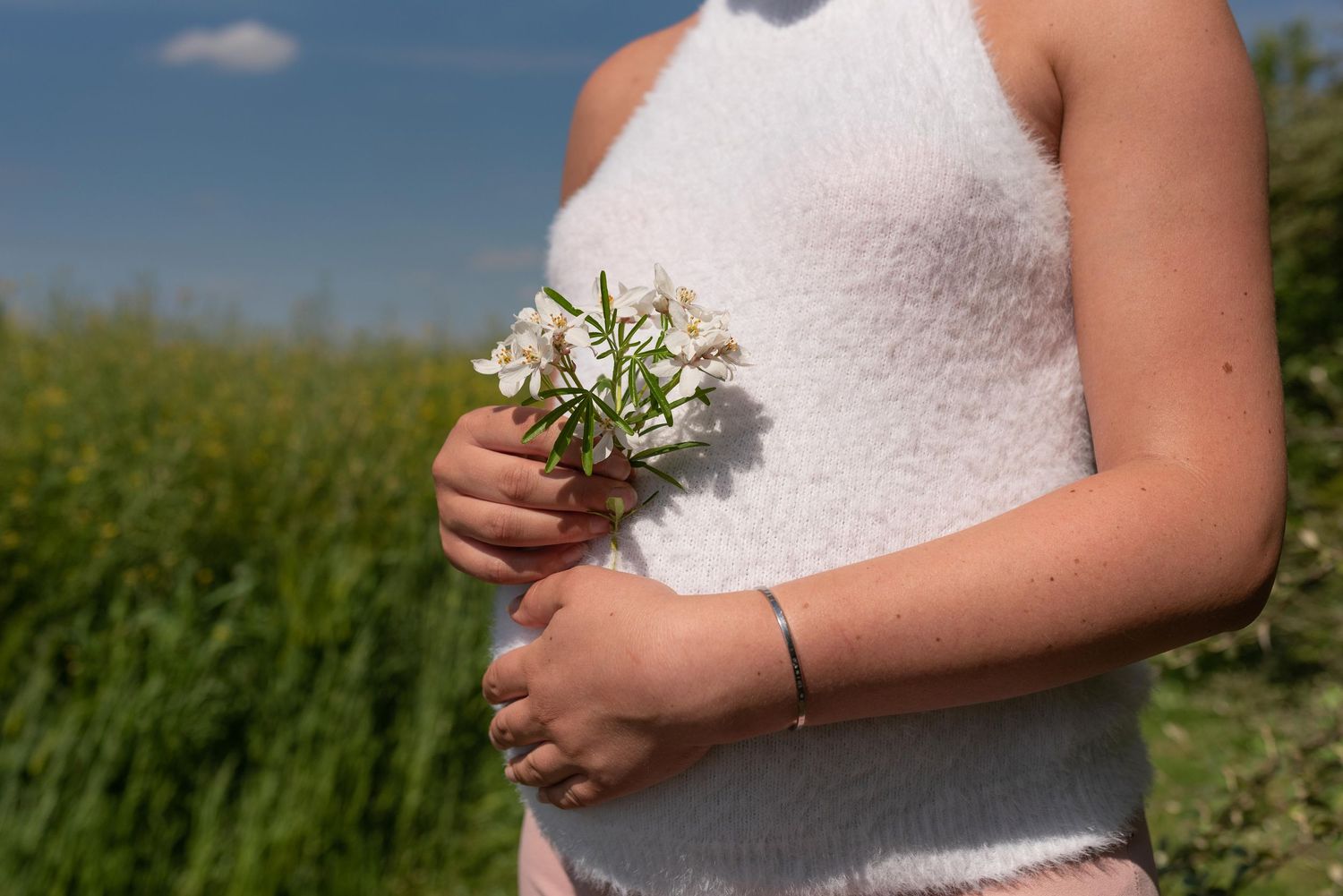 Jeune femme en haut blanc tenant des fleurs sauvages blanches dans un champ verdoyant par une journée ensoleillée
