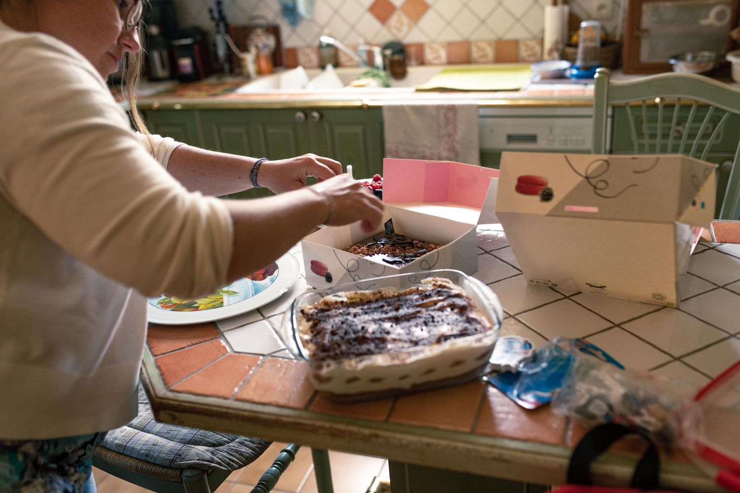 Une femme sert un dessert au chocolat, sorti d'un plat à four, sur un comptoir de cuisine carrelé, avec des cartes de vœux à proximité.
