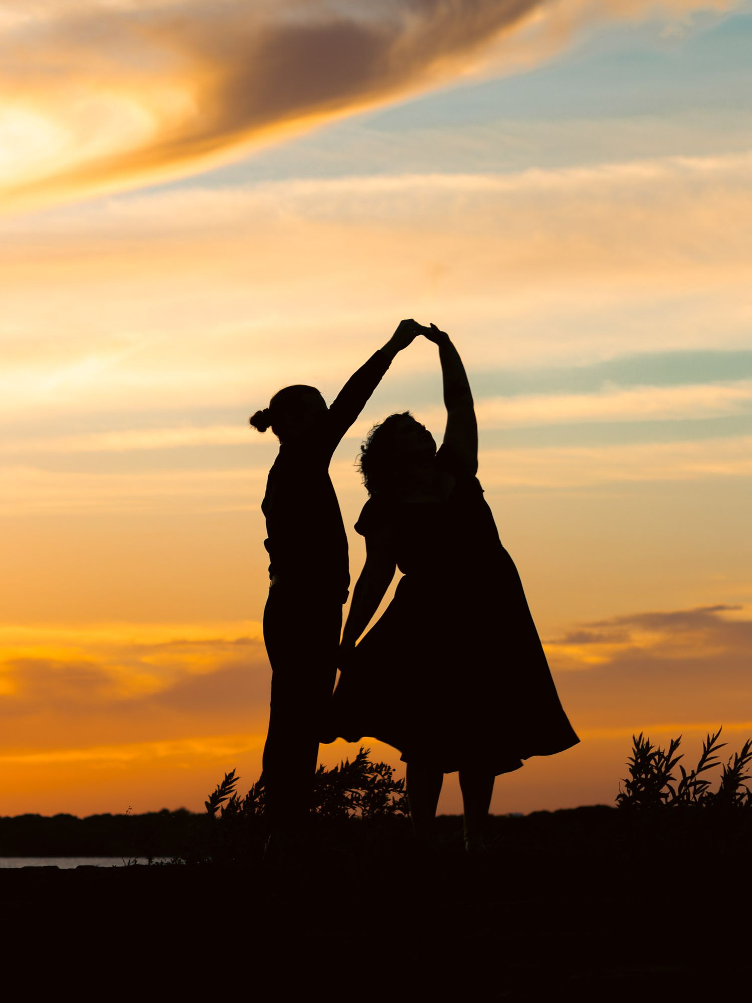 Silhouette of two people dancing and holding hands against a vibrant golden sunset sky.