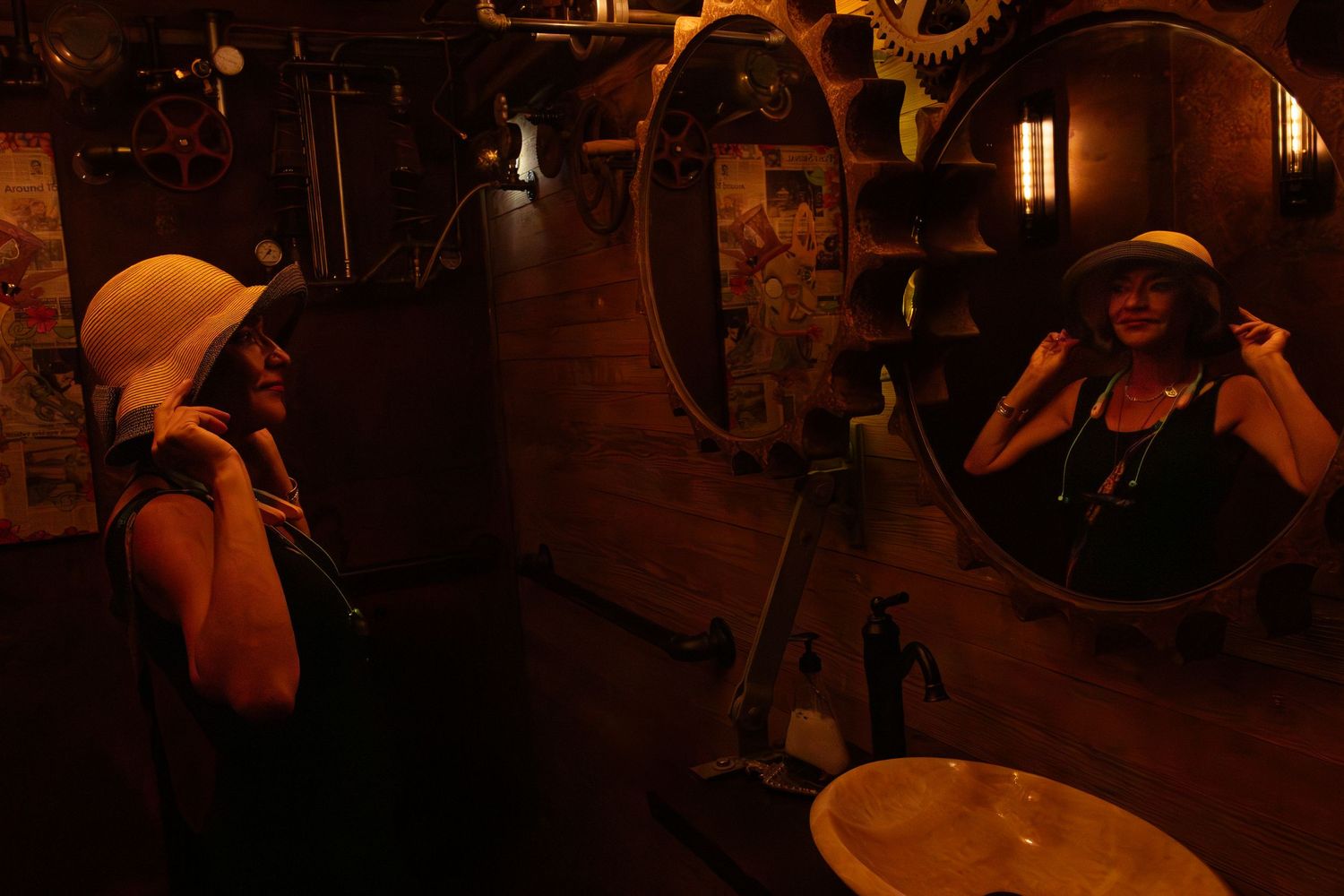 Woman in vintage 1920s flapper style adjusting yellow hat while looking in round mirror in dimly lit room.
