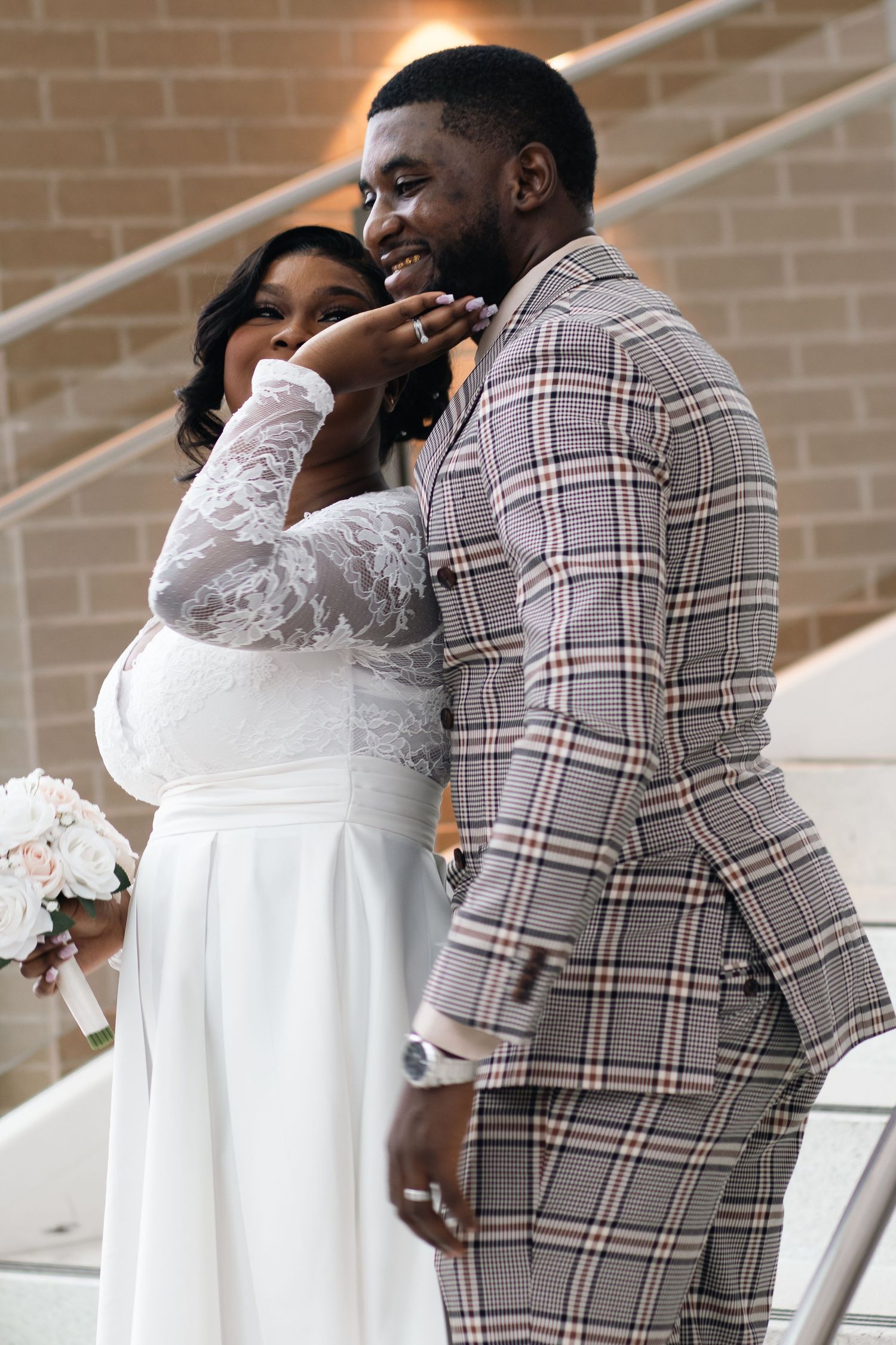 Playful and luminous moment of a bride touching her groom's face on a staircase after their micro-wedding.