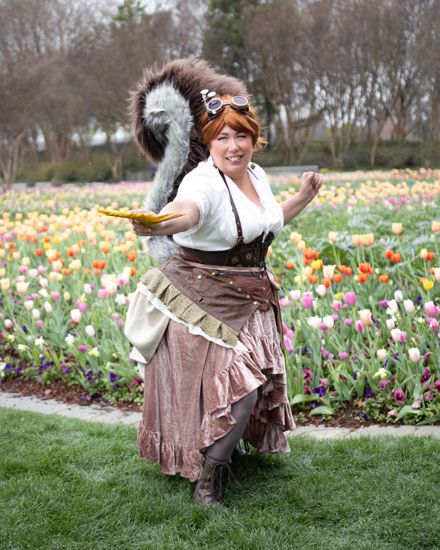 Woman in steampunk costume with squirrel tail poses in colorful tulip garden.