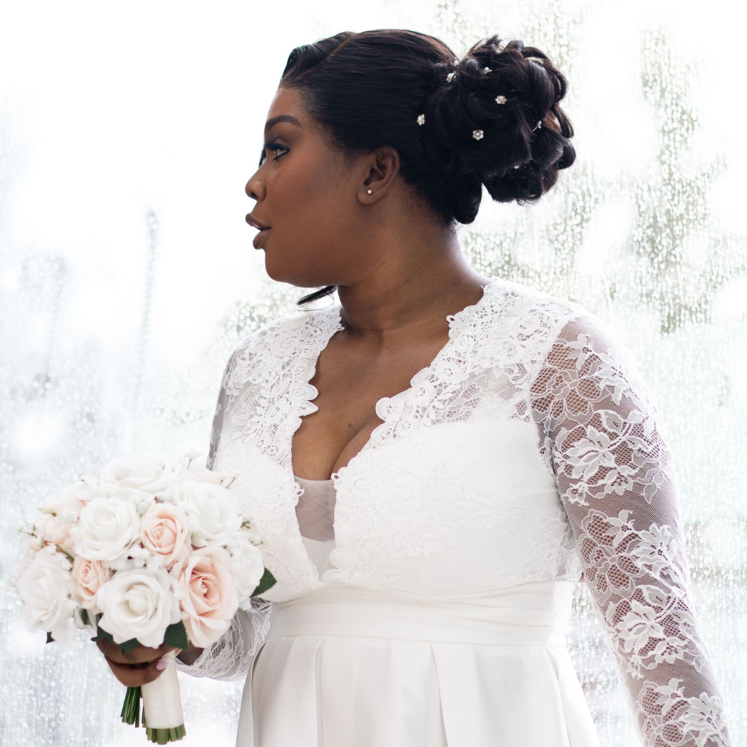 Elegant bride in lace long-sleeve wedding gown holding blush pink rose bouquet with pearl hair accessories.