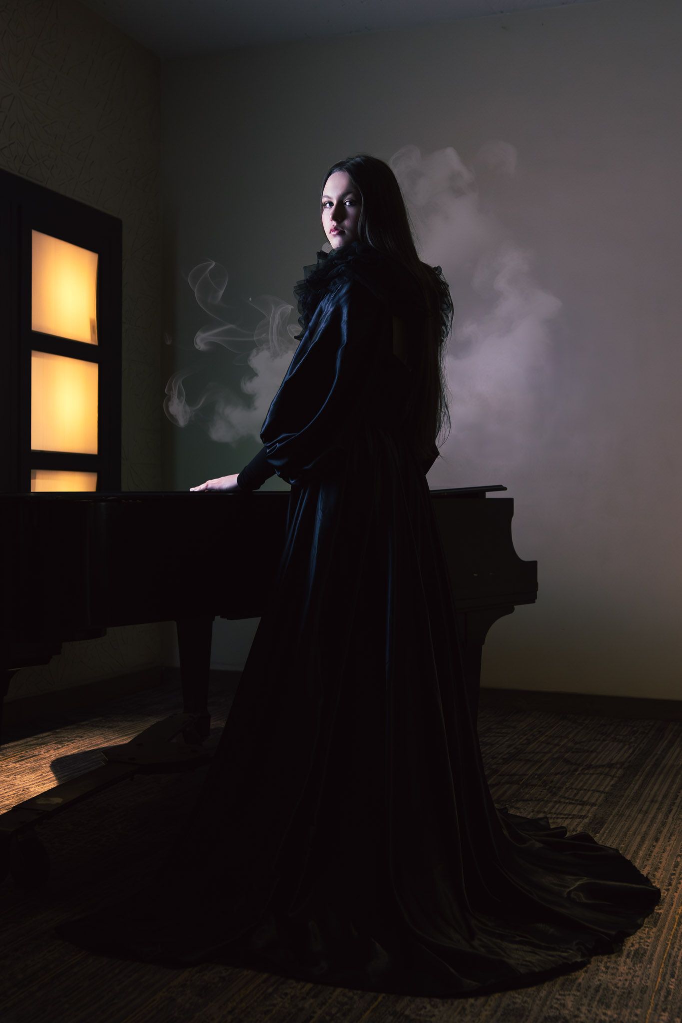 Woman in dark velvet gown stands beside a grand piano in a dimly lit smoky room.