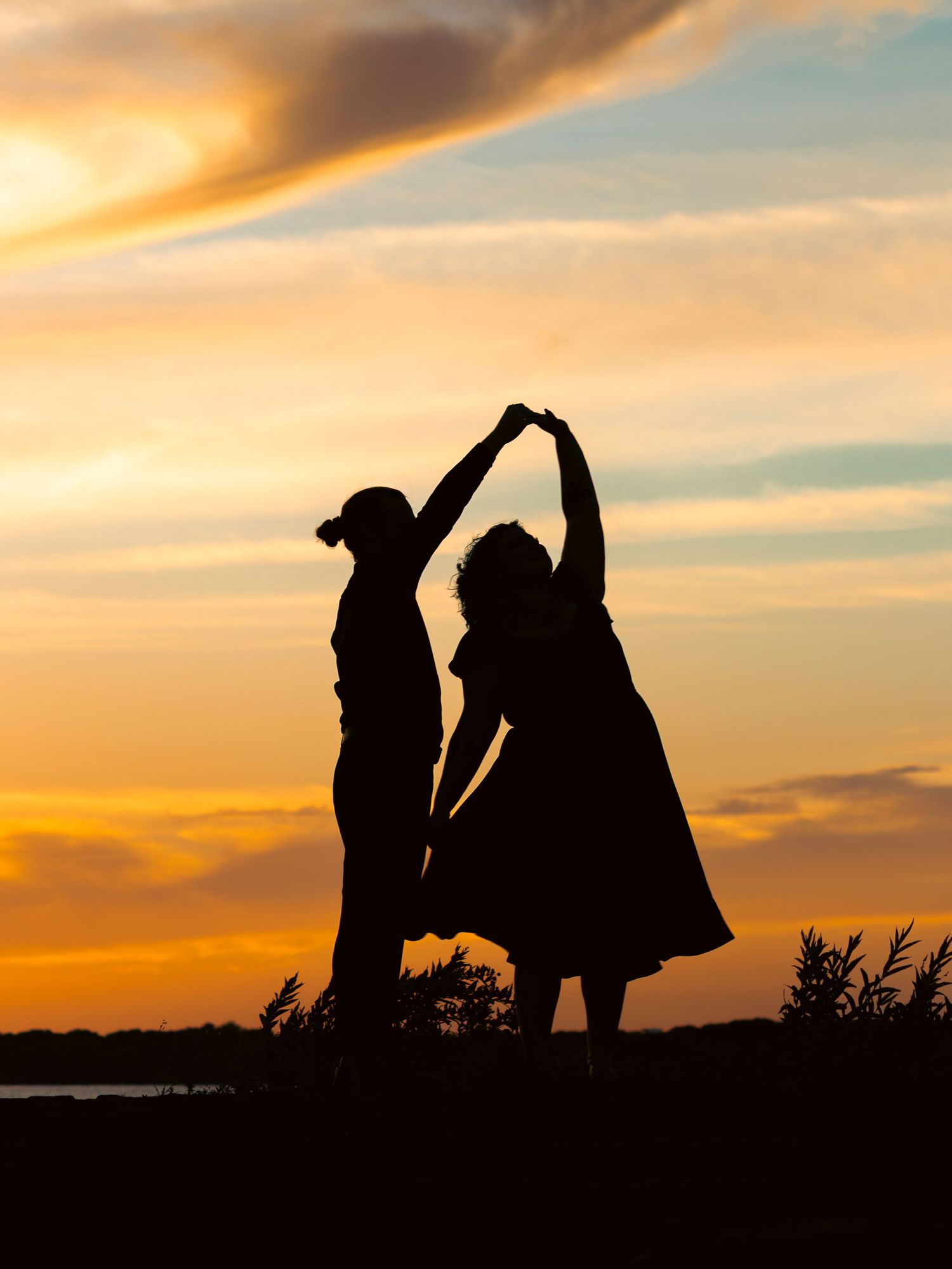 Silhouette of two people dancing together at sunset with vibrant orange and golden sky backdrop.