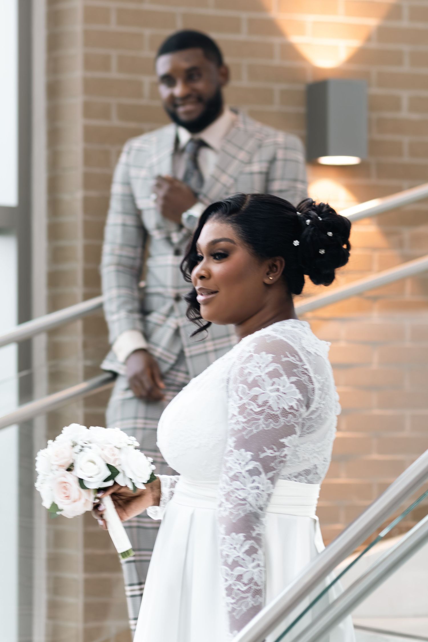 Bride in lace wedding dress holding bouquet with groom in plaid suit on stairs.