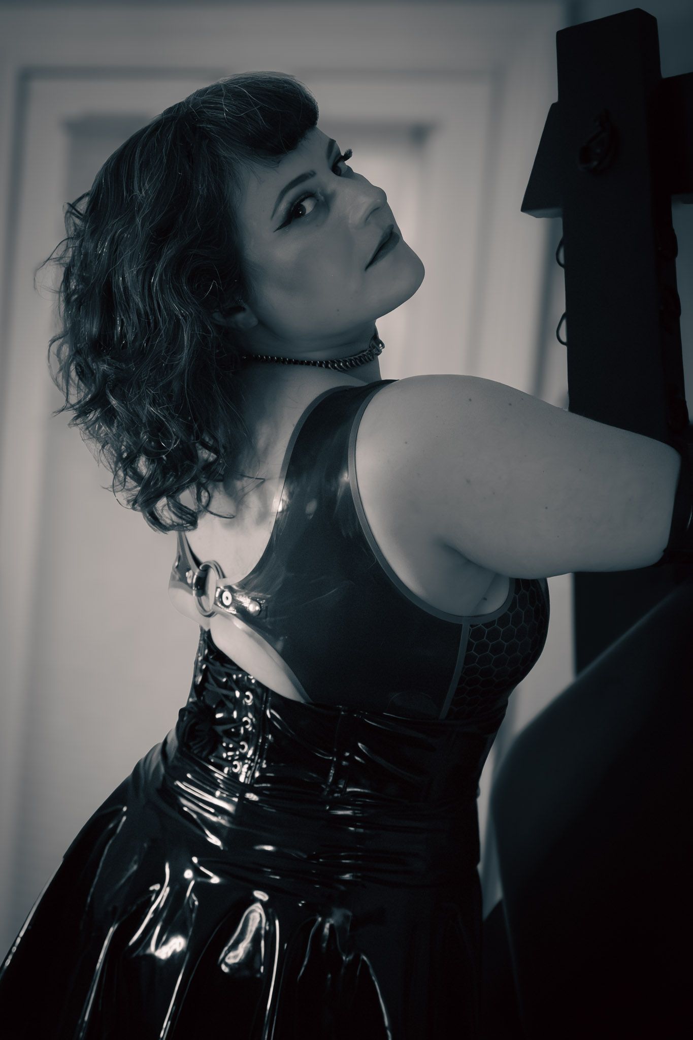 Woman in shiny black latex dress poses dramatically in monochrome portrait photography.