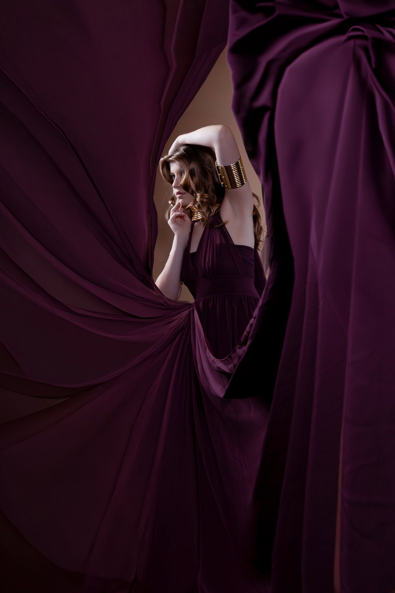 Woman in elegant burgundy gown surrounded by flowing purple drapes, posing gracefully in a dramatic fashion editorial.
