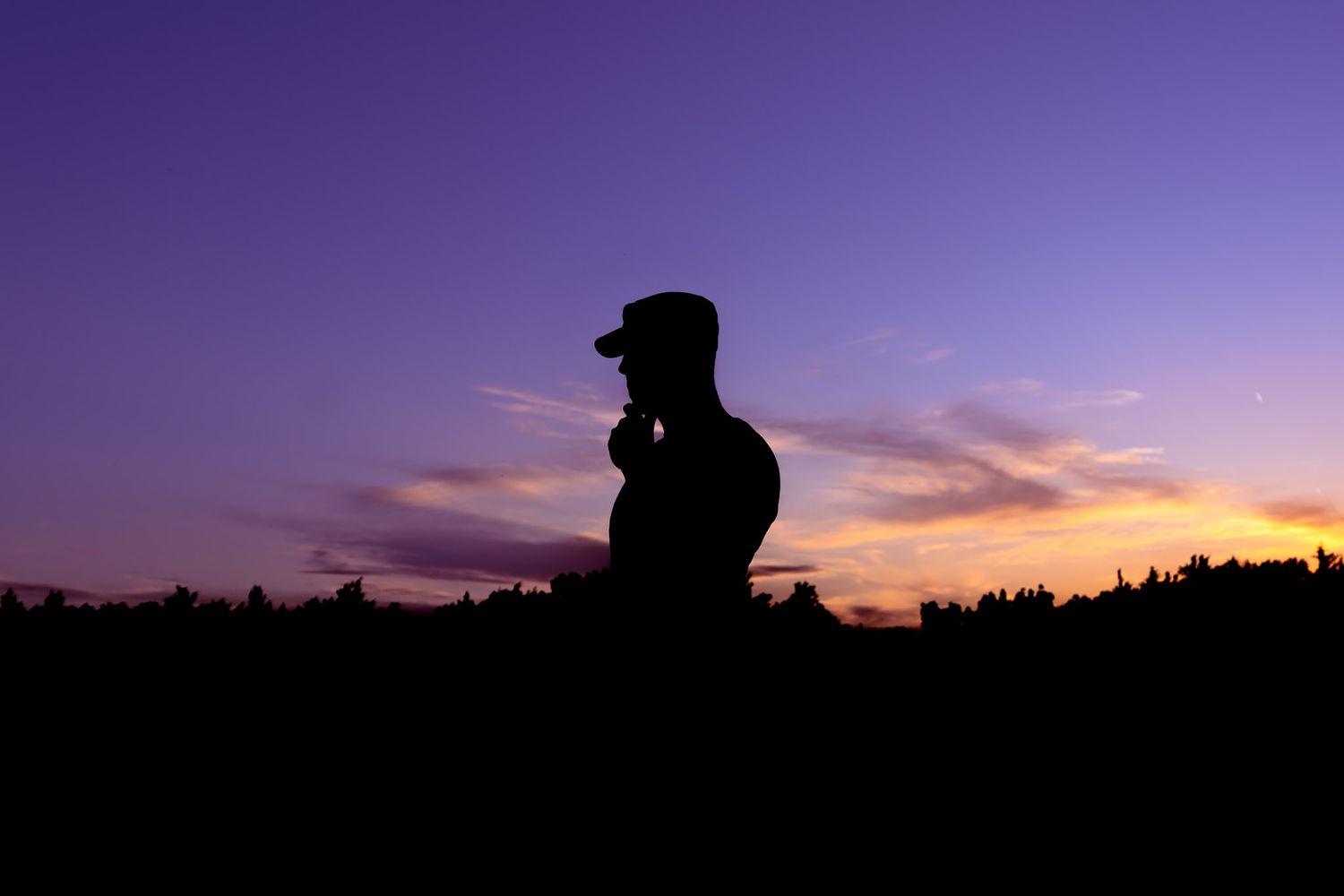 Silhouette of a person wearing a cap against a vibrant purple and orange sunset sky.