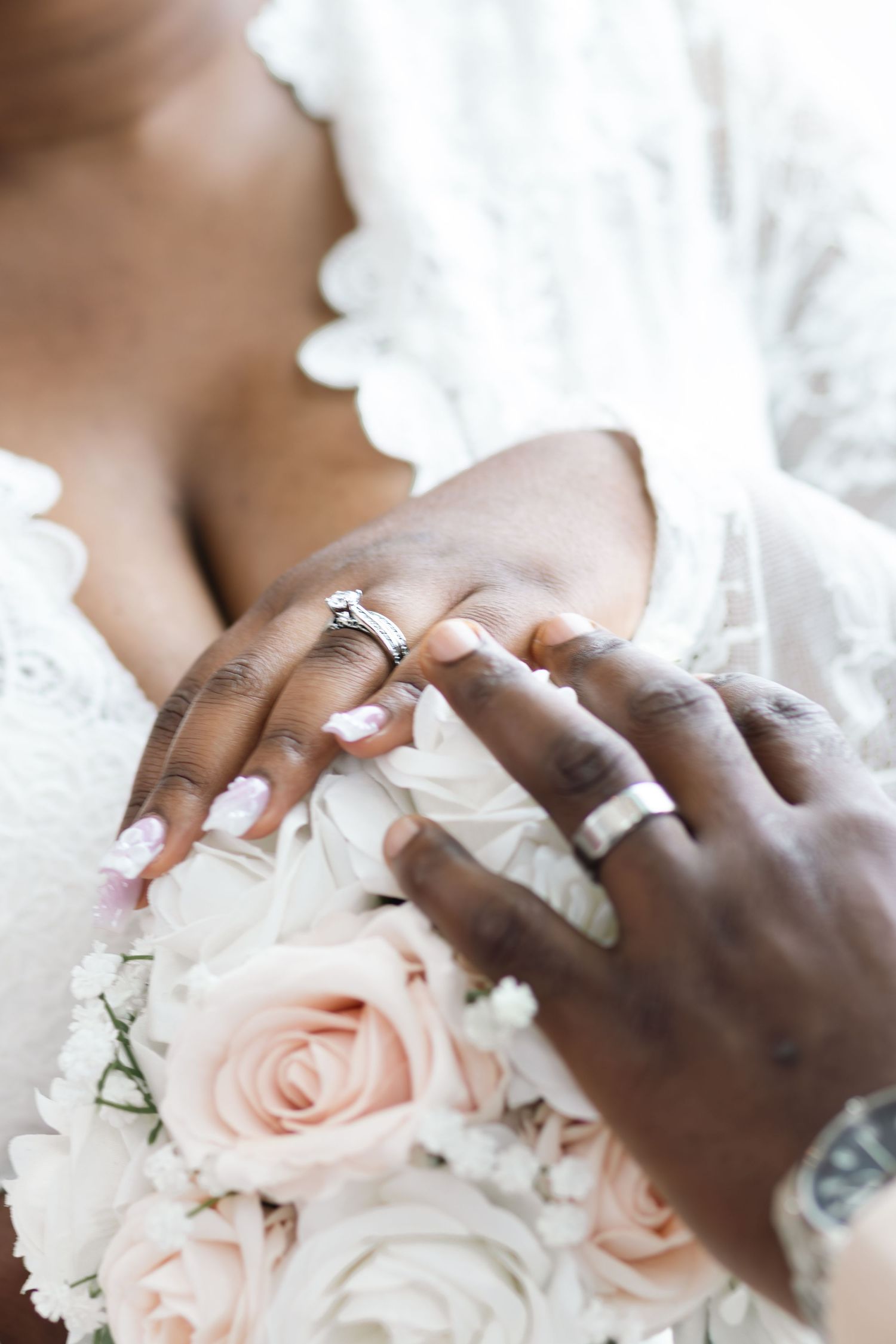 Newlywed couple's hands with wedding rings resting on a bouquet of blush pink roses.