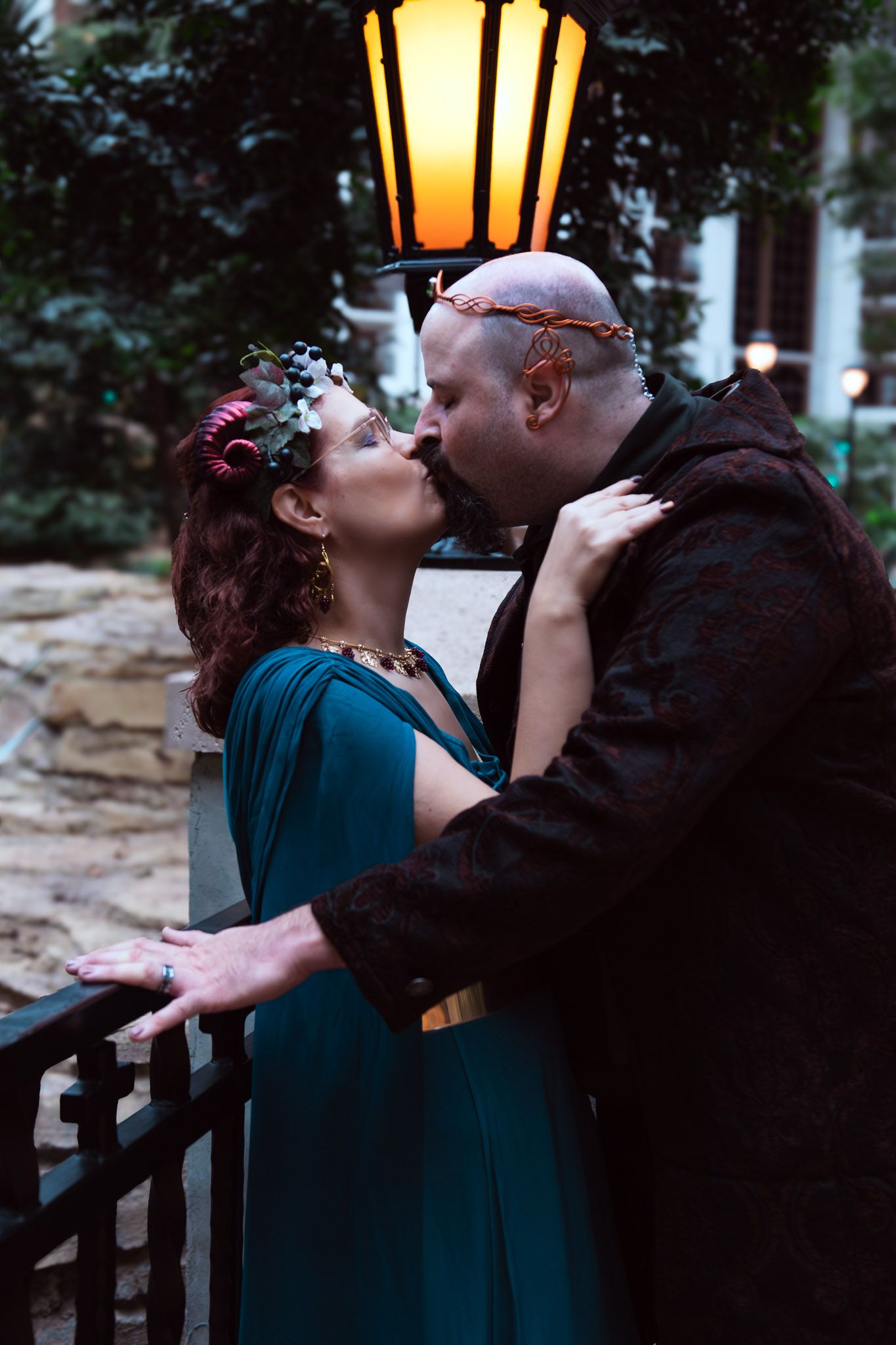 Couple in fantasy elf costumes sharing a romantic kiss under a glowing lantern outdoors.