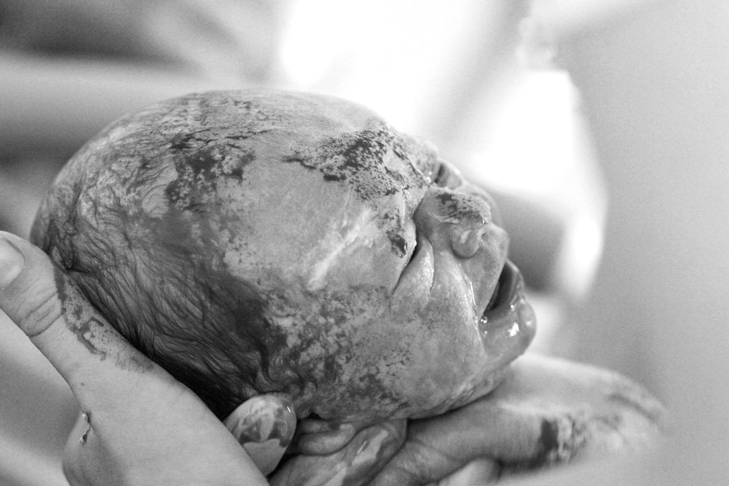 A newborn seconds after birth still covered in blood. The Mother's Eye - documentary home birth photography Camberwell, London.