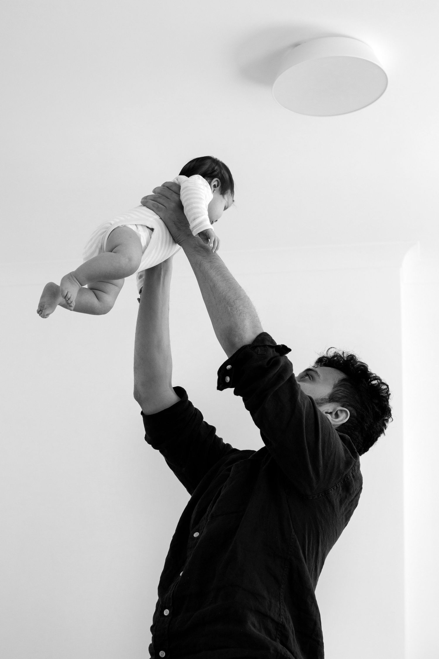 Father lifts up his baby in black and white. Family and childhood photographer The Mother's Eye in Beckenham, South East London.