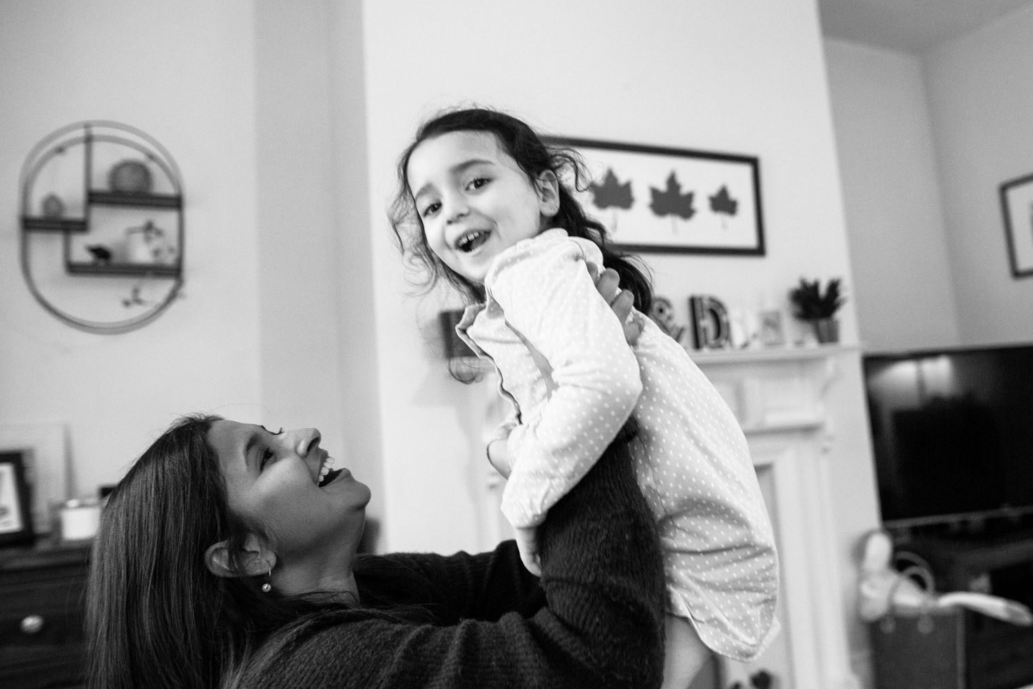 A mother lifts her daughter laughing. The Mother's Eye - fun documentary-stele motherhood photography in Bermondsey, London.