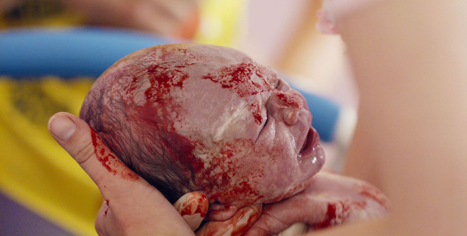 A newborn seconds after birth still covered in blood. The Mother's Eye - candid documentary-stele home birth photography Bermondsey, London.