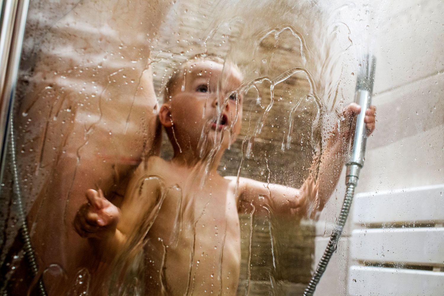 A toddler sprays water around the shower cabin. Wild childhood documentary sessions, fun, full of emotions by The Mother's Eye, Camberwell.