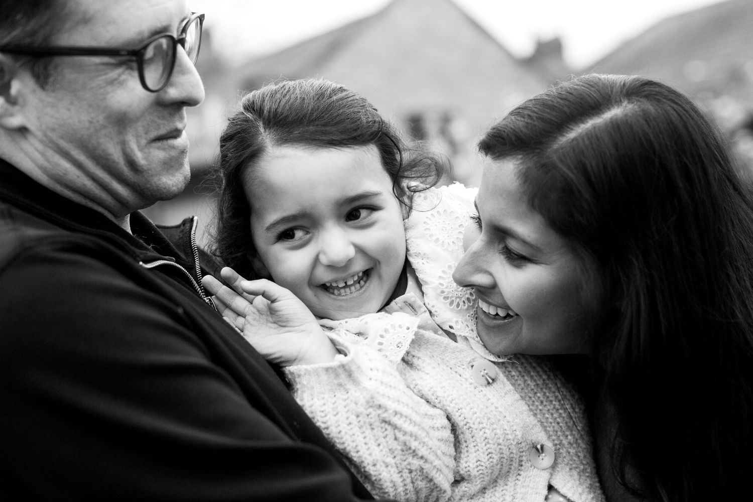 Mum, dad and a 3 year old girl cuddling outdoors in black and white. Family and childhood photoshoot Greenwich, South East London.