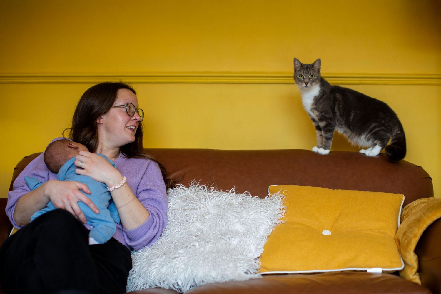 Mum sits on a sofa with her newborn looking at a cat. Postpartum and Fourth Trimester photography The Mother's Eye, Crystal Palace,  London.