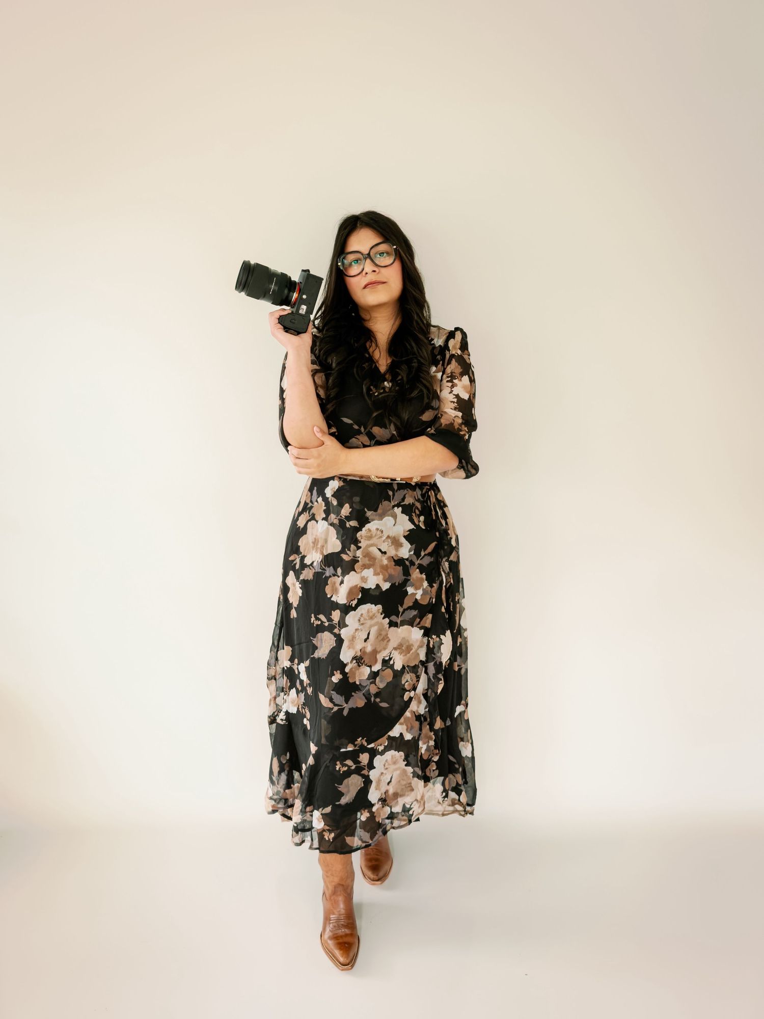 Woman photographer in floral dress holding camera in studio.