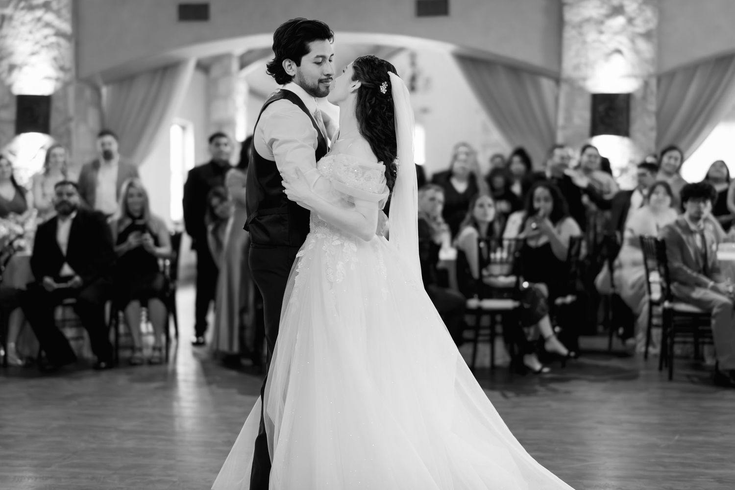 Black and white photo of newlyweds sharing intimate first dance in elegant draped reception ballroom.