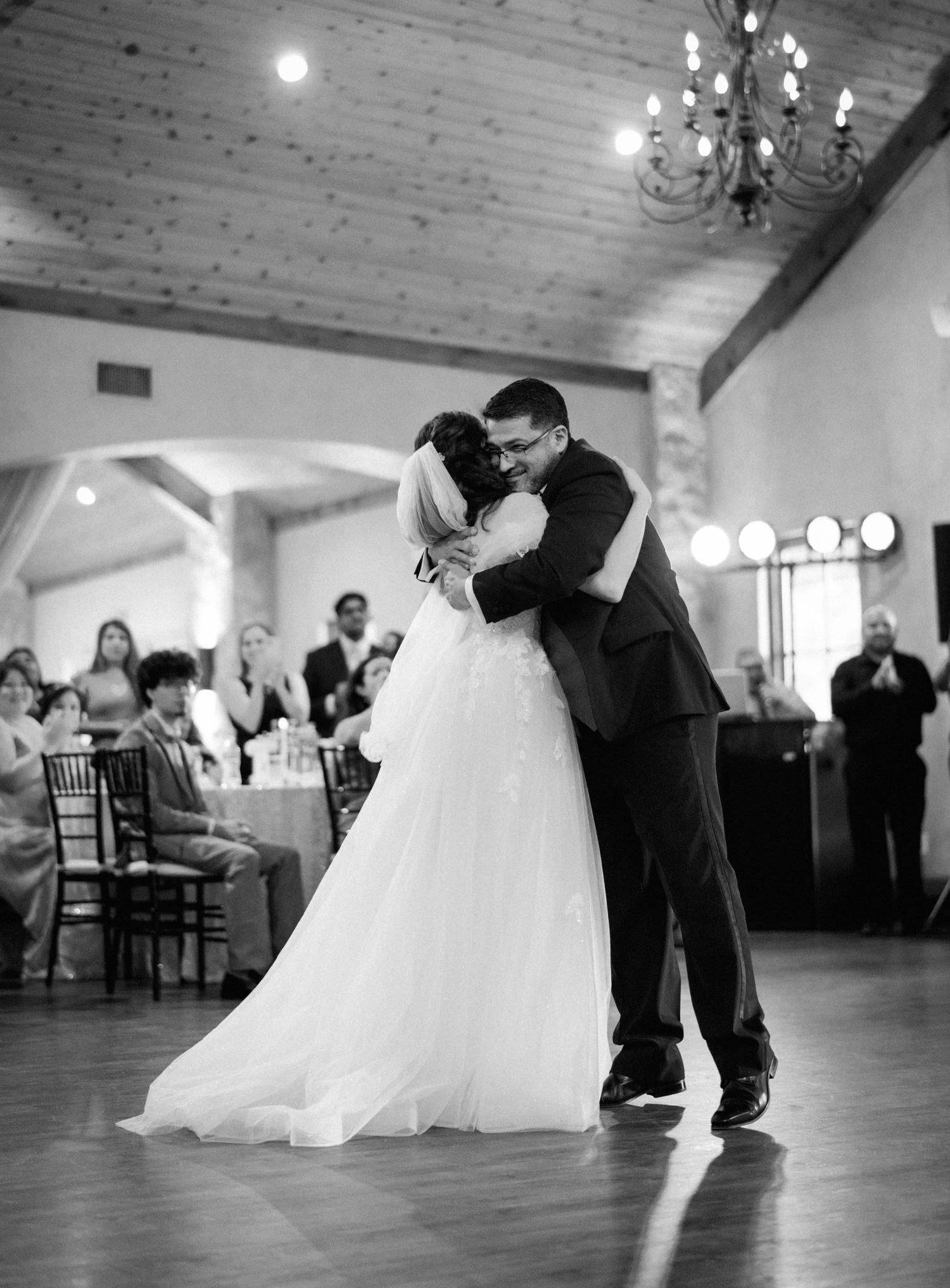 Black and white photo of bride and groom sharing emotional first dance embrace at wedding reception.