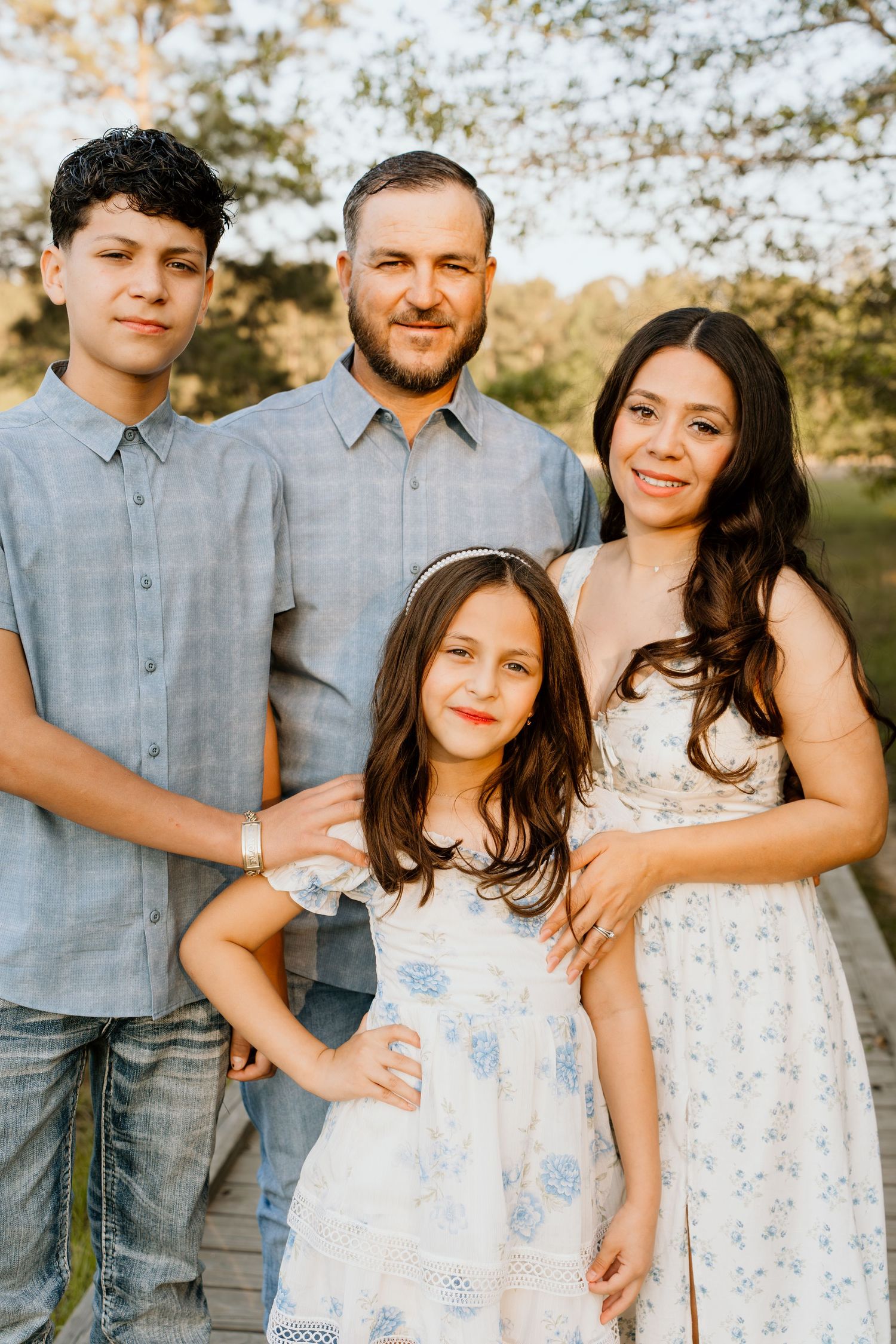 A happy family of four poses outdoors in golden light, wearing coordinated blue and white outfits for a portrait.