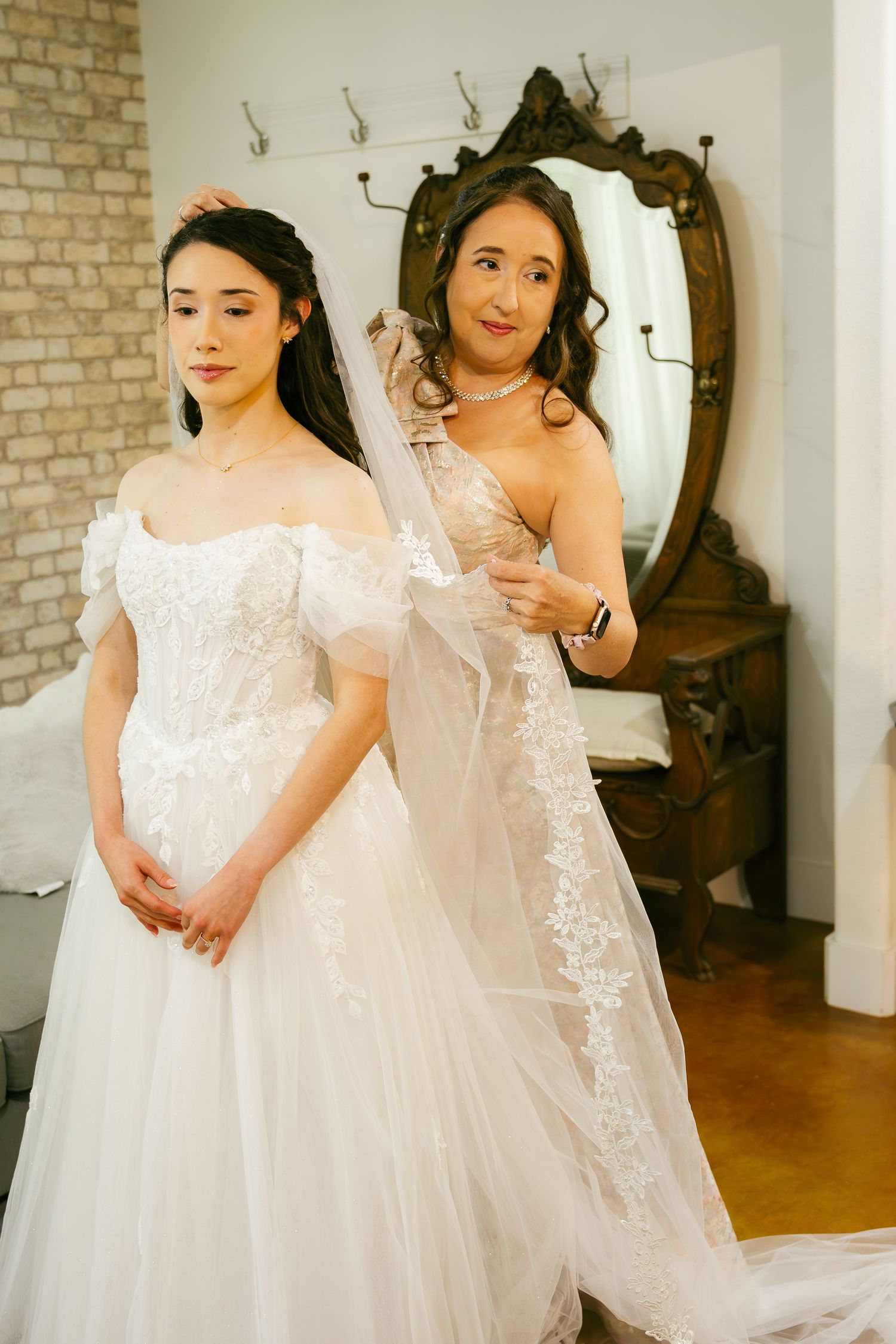 Mother helping bride into her off-shoulder lace wedding gown before the ceremony.