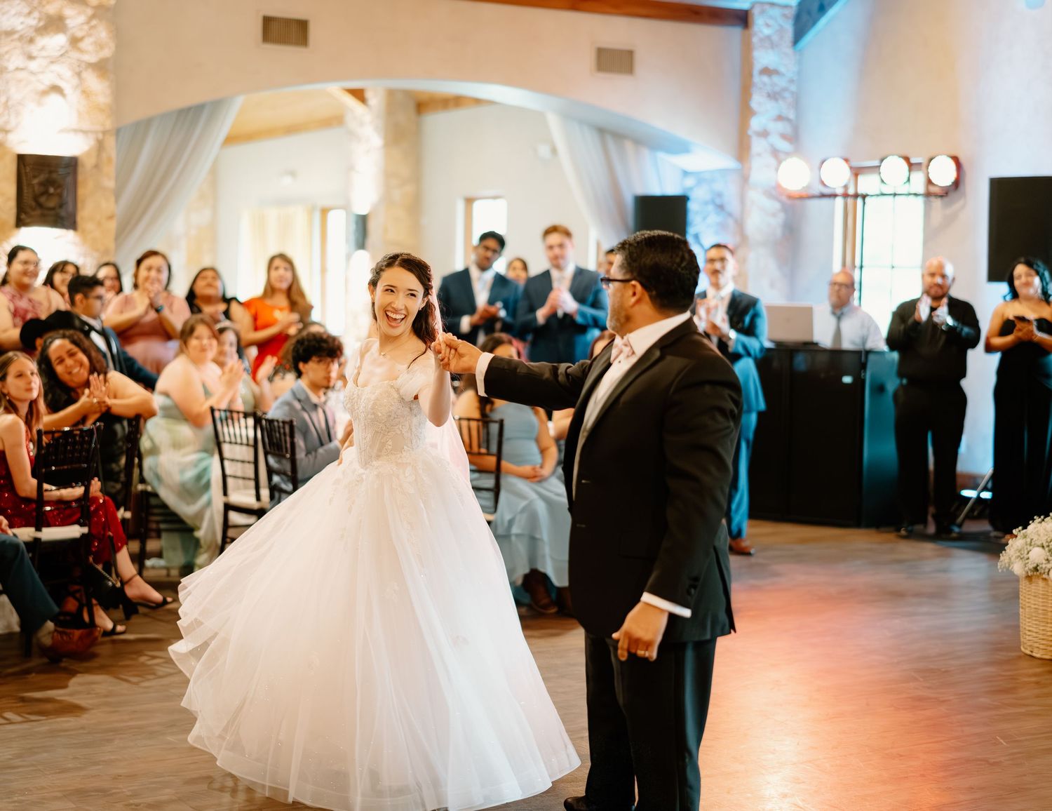 Bride and groom share first dance at elegant wedding reception surrounded by applauding guests.