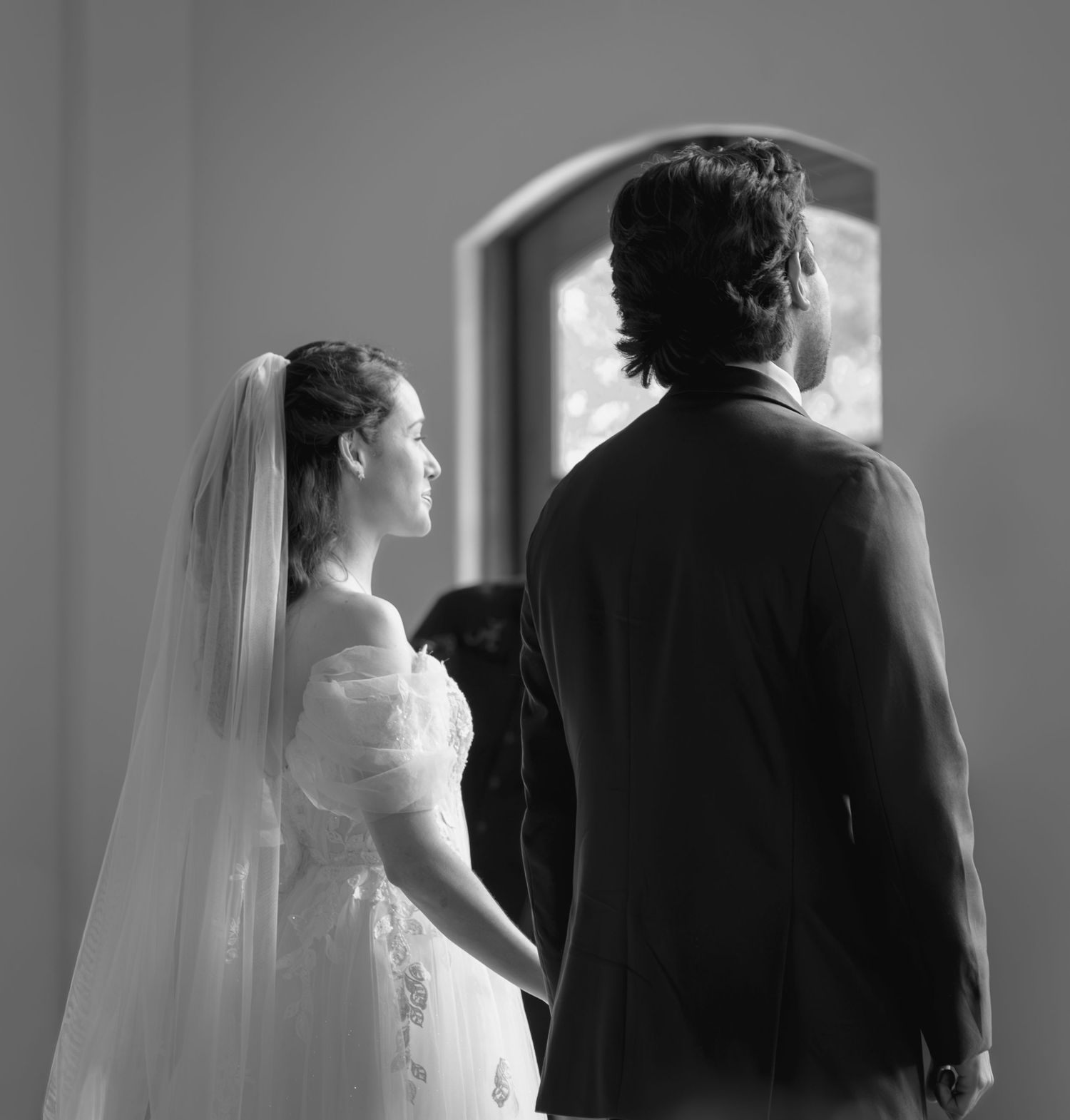 Black and white photo of a bride and groom holding hands at the altar during their wedding ceremony.