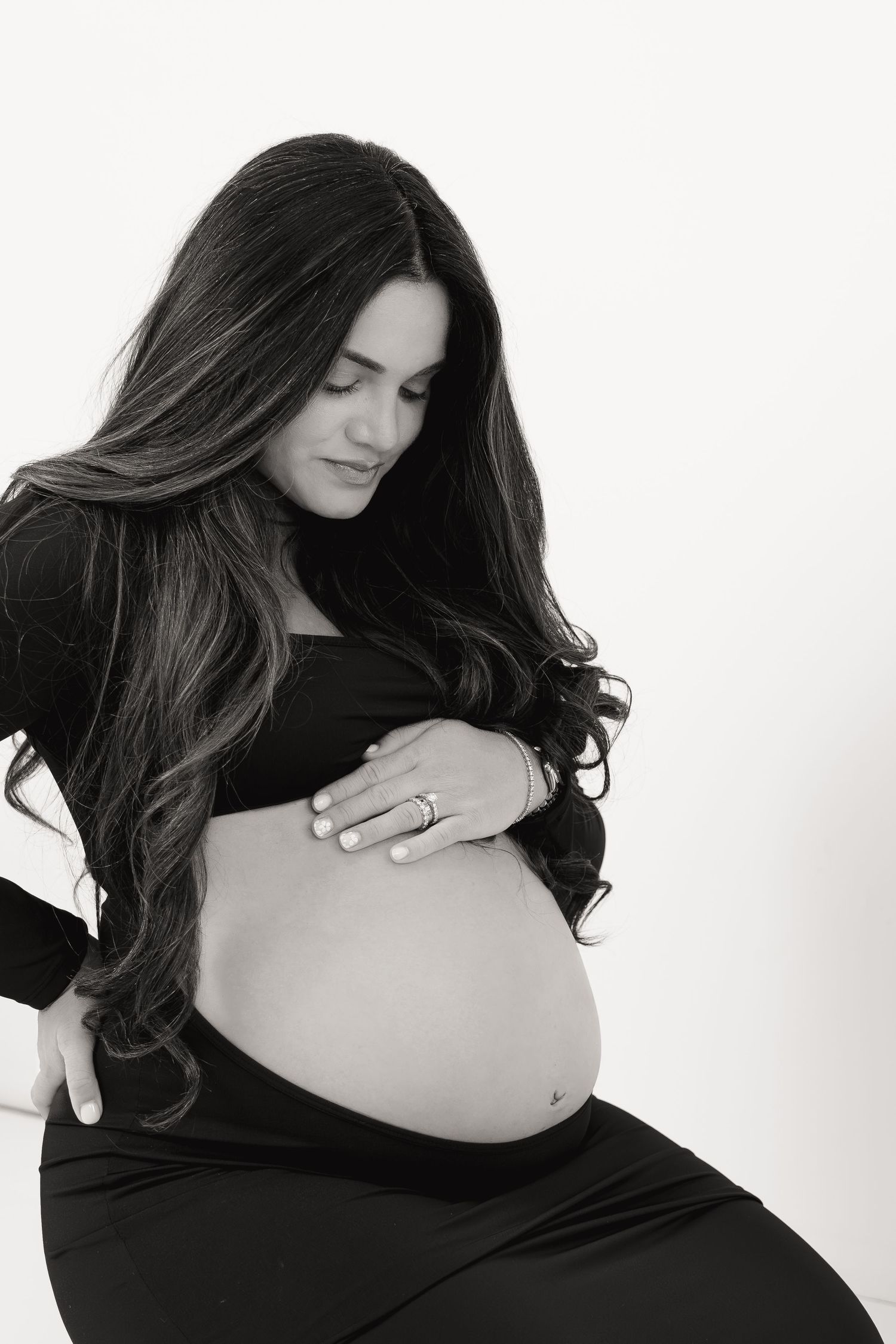Black and white maternity photo of pregnant woman in black dress gently holding her baby bump.