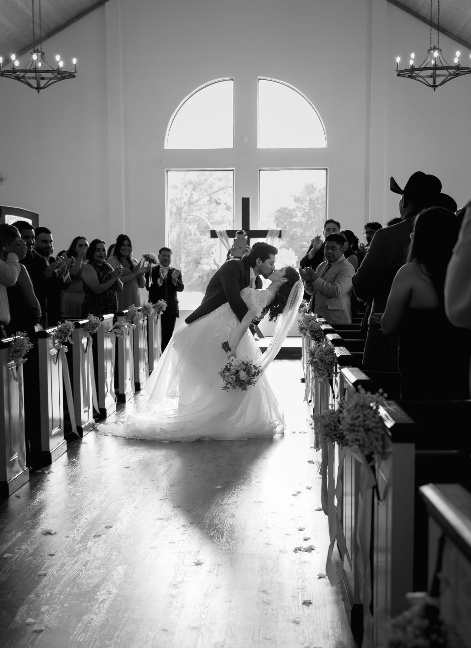 Black and white photo of a bride and groom sharing a first kiss at the altar in a white chapel.