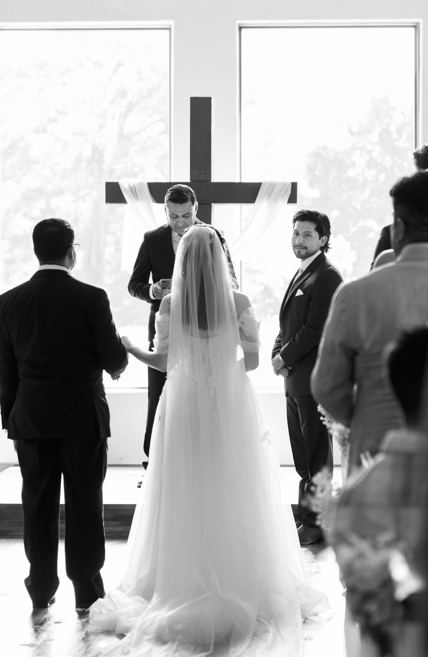 Bride and groom exchanging vows before a wooden cross in a white chapel ceremony.