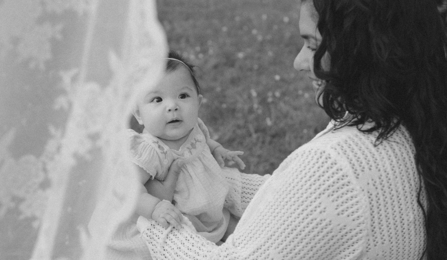 Black and white photo of a mother in white sweater tenderly holding her newborn baby outdoors.