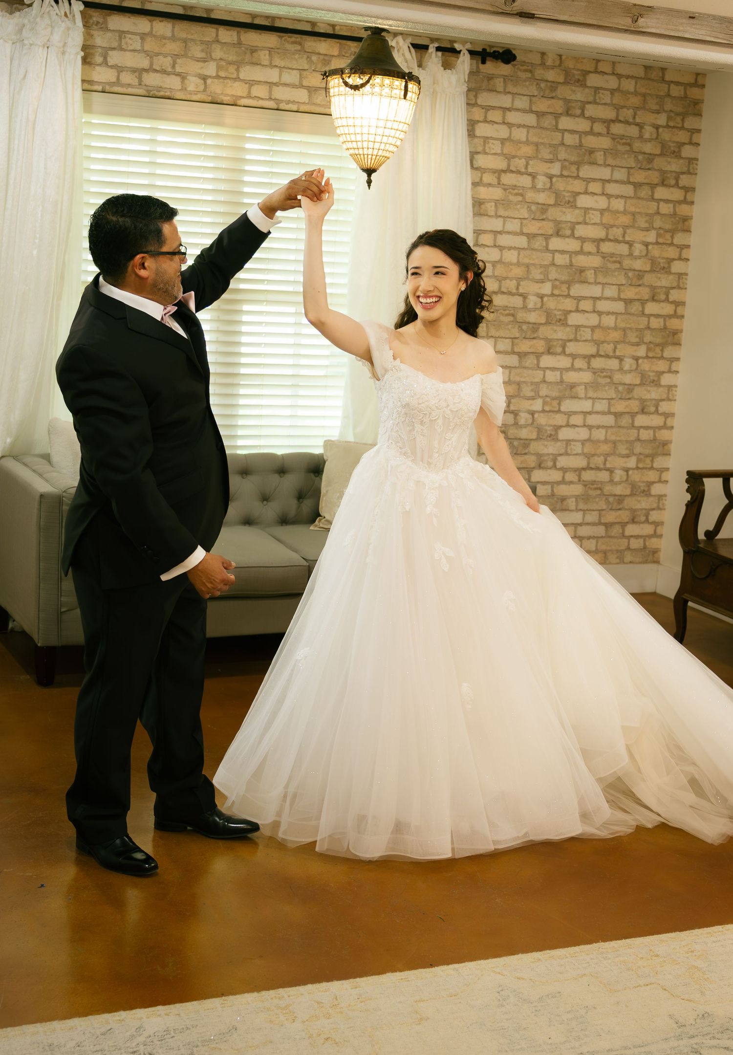 Bride in a white ball gown twirls with a man in a black tuxedo during a wedding dance in an elegant venue.