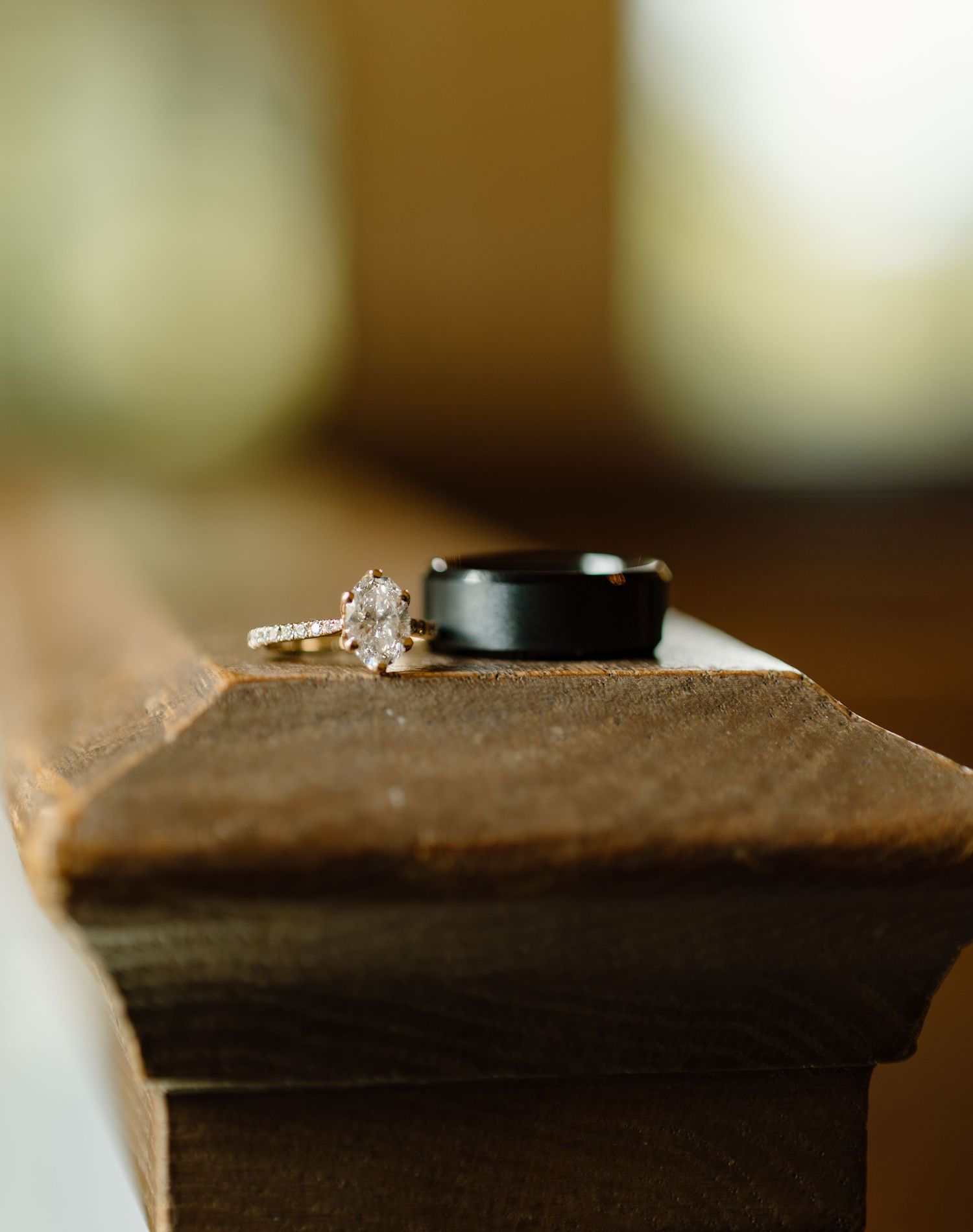 Gold diamond engagement ring and black wedding band displayed on wooden surface for elegant wedding jewelry detail shot.