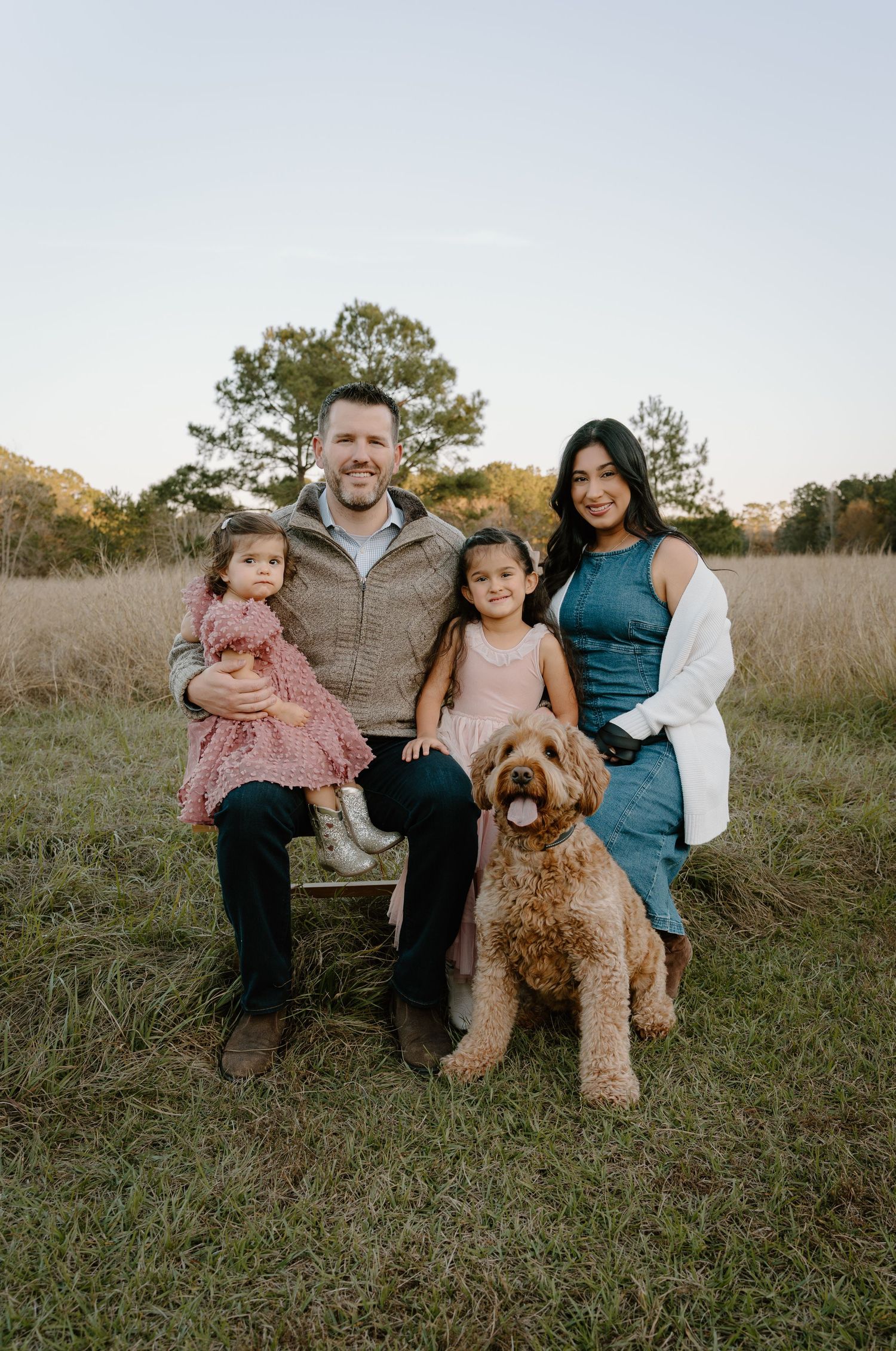 Family of four with a golden doodle dog posing outdoors in a grassy field during golden hour.