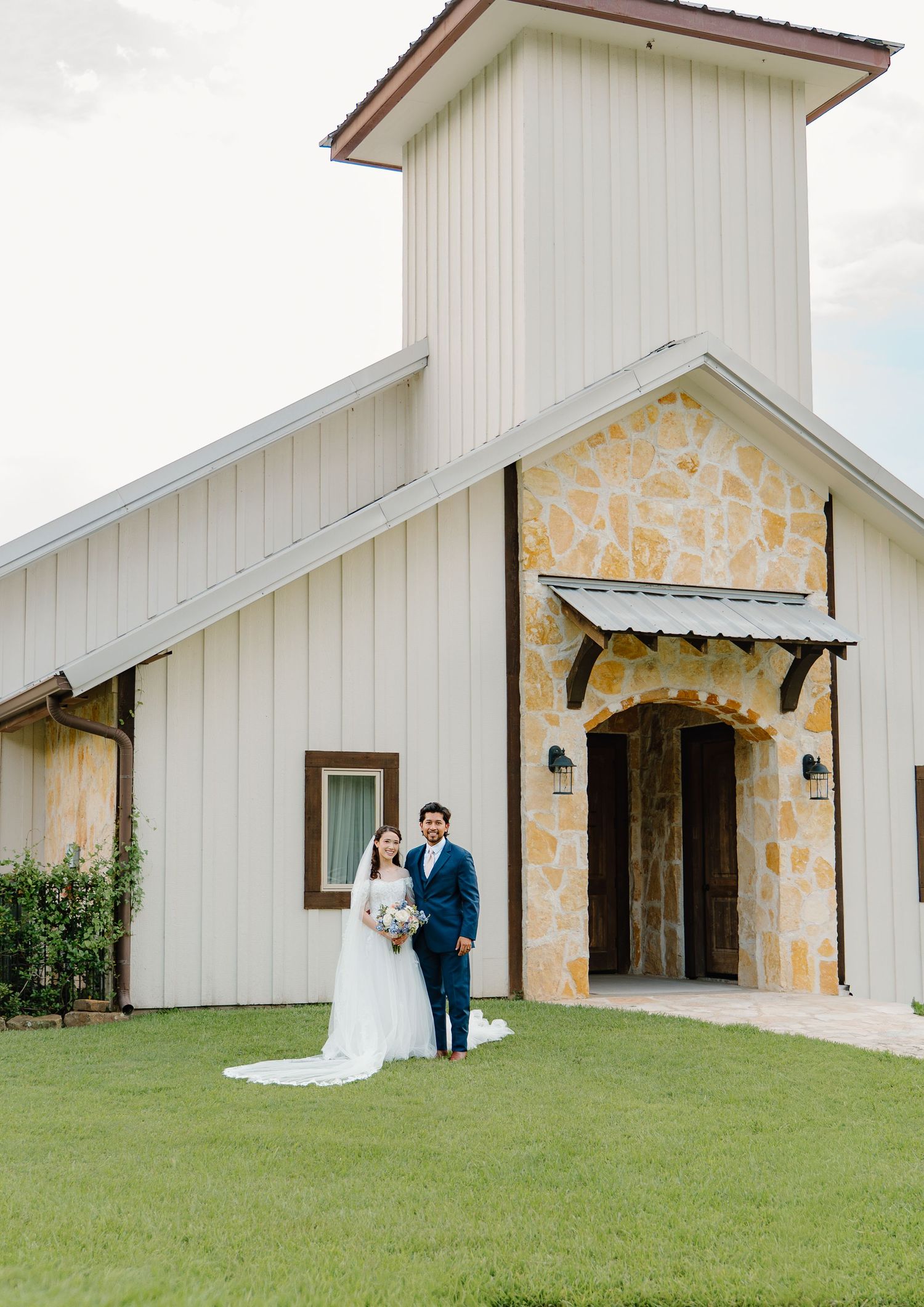 Bride and groom standing together outside a white stone chapel on their wedding day.