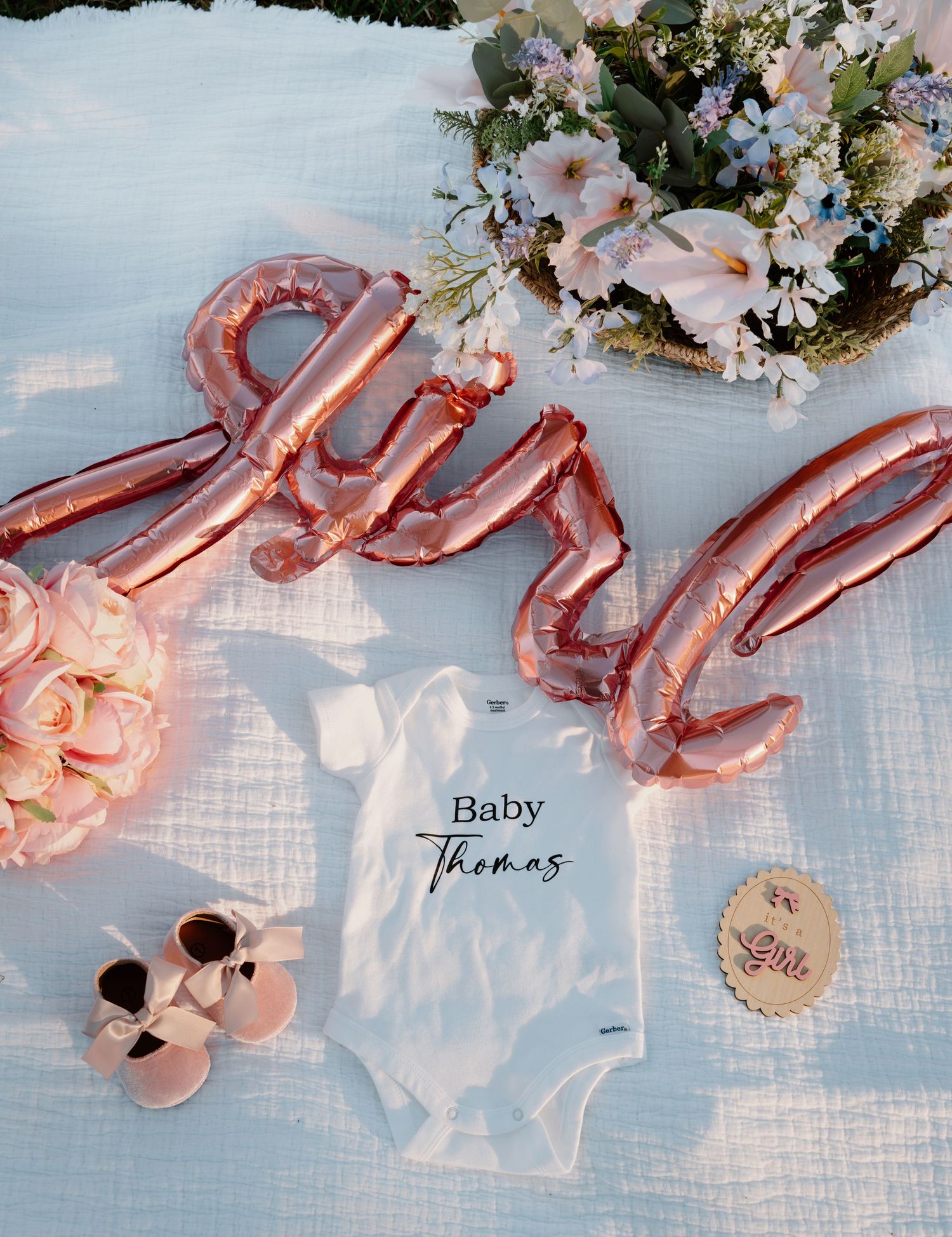 Baby girl gender reveal flat lay with rose gold balloons, pink shoes, and white onesie.