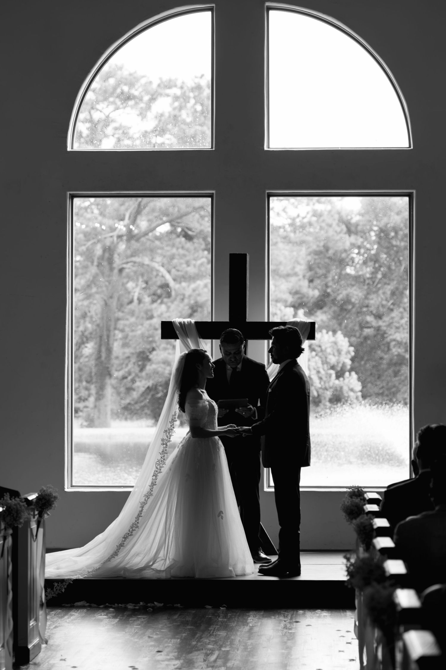 Silhouette of bride and groom at the altar framed by arched chapel windows.