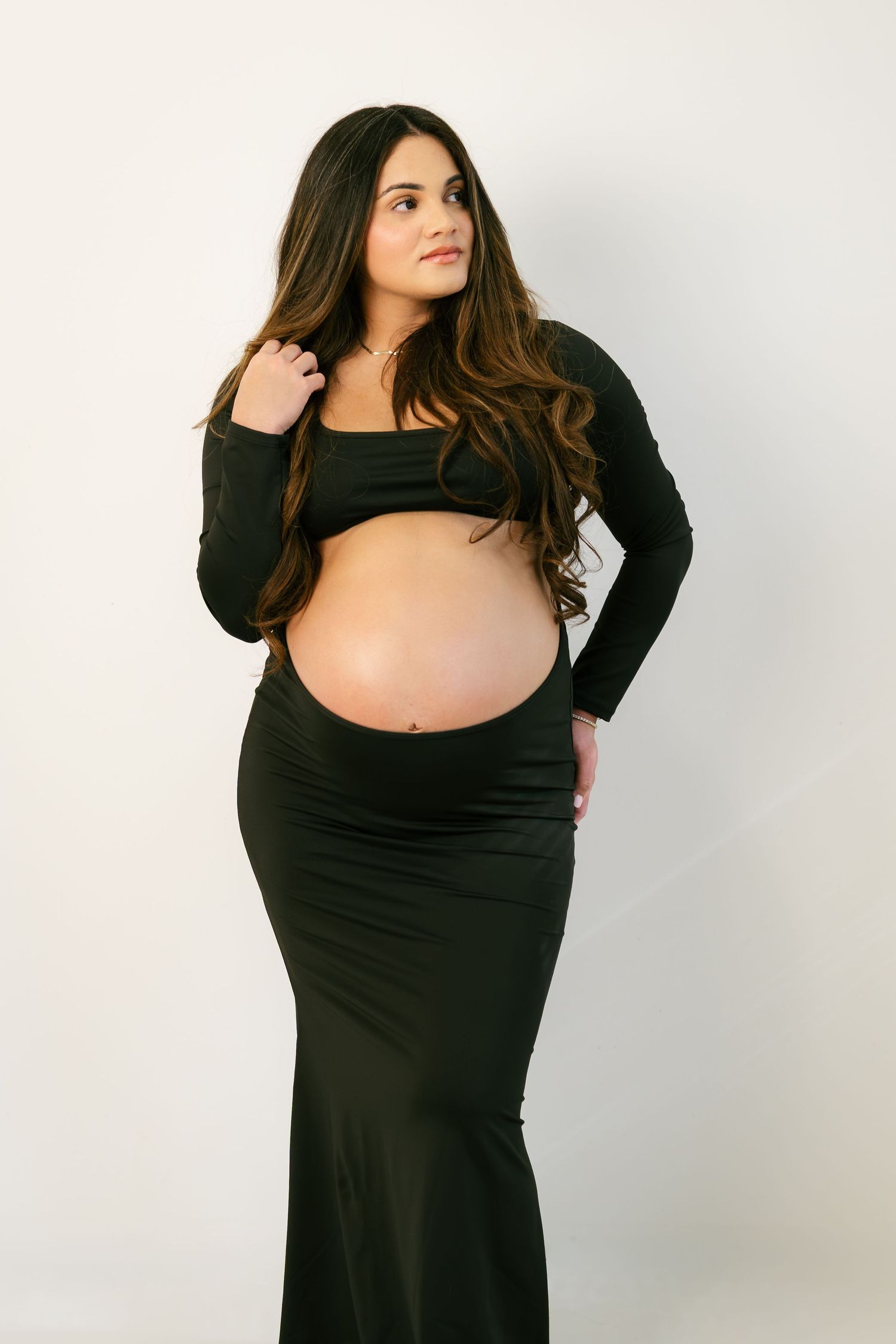 Pregnant woman in black crop top and maxi skirt showing baby bump in studio photo.