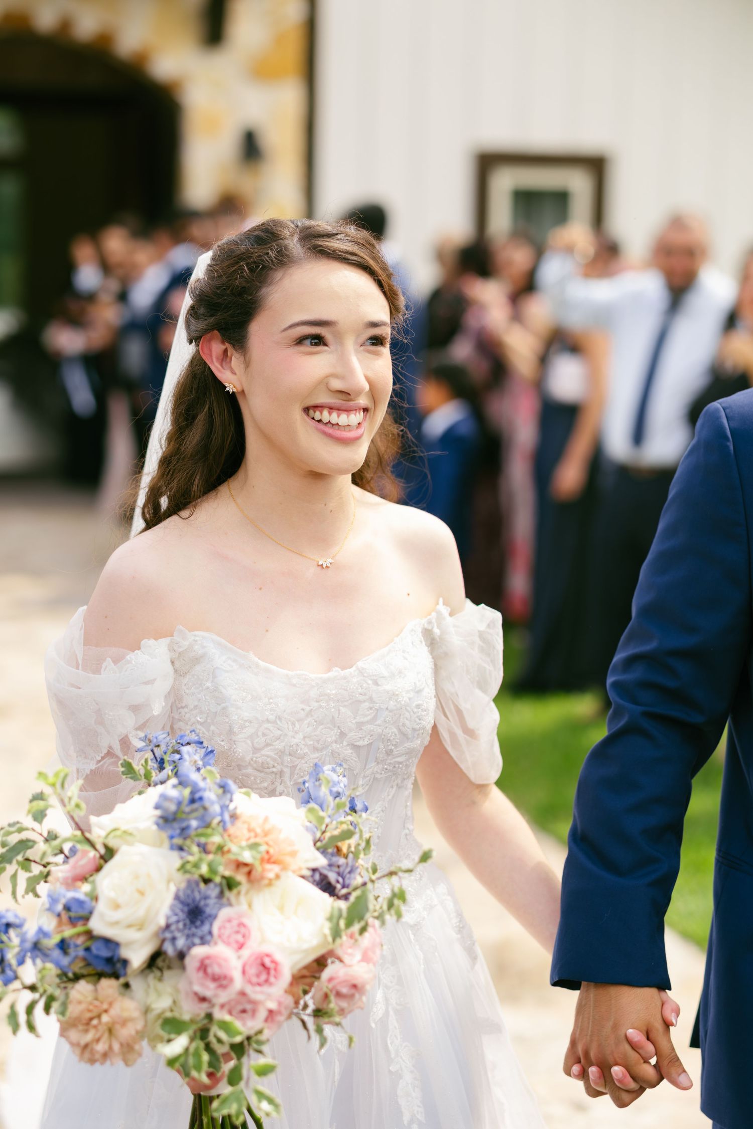 Radiant bride smiling while holding a colorful bouquet of pink and blue flowers.
