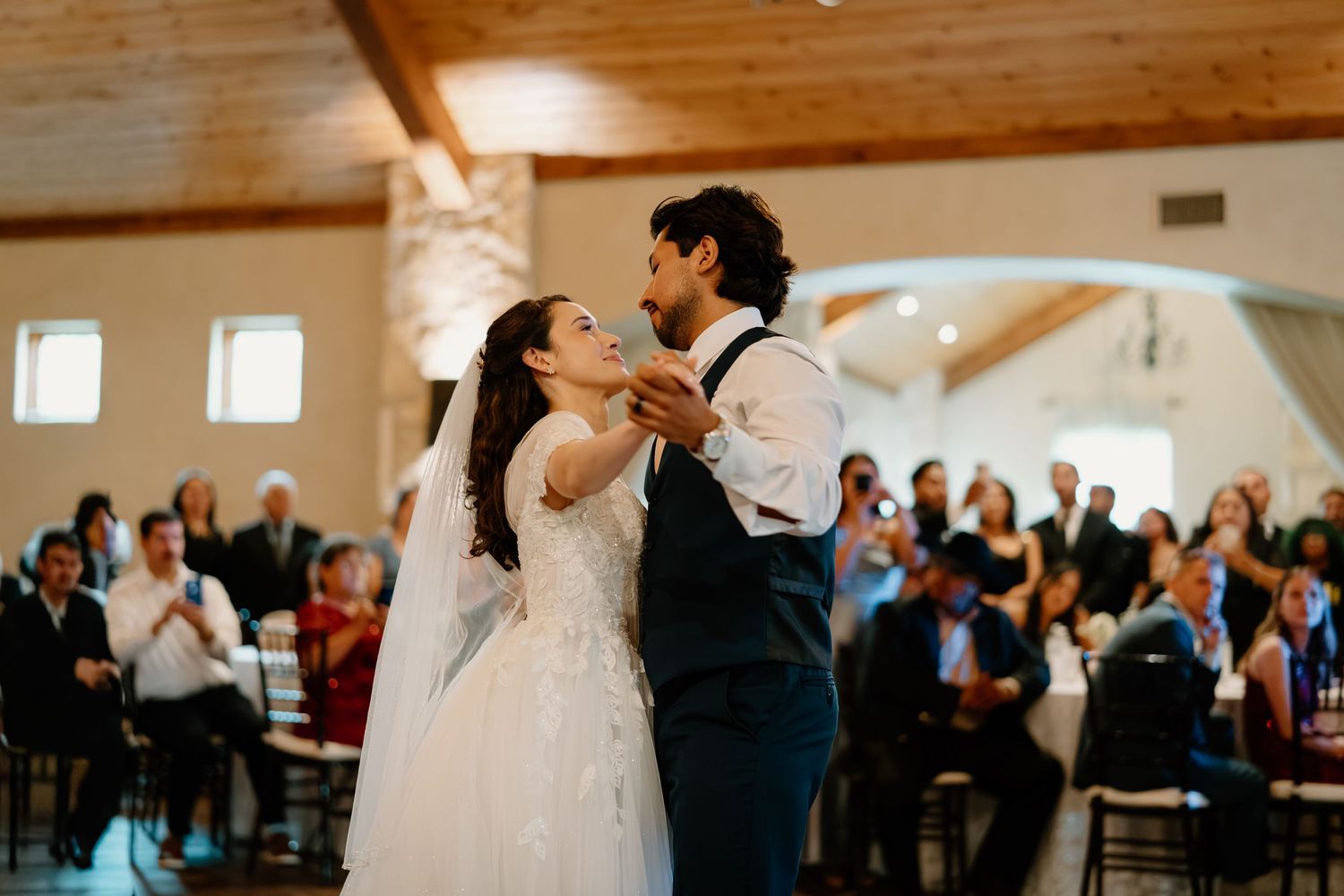 Bride and groom sharing their first dance before cheering guests at the reception.